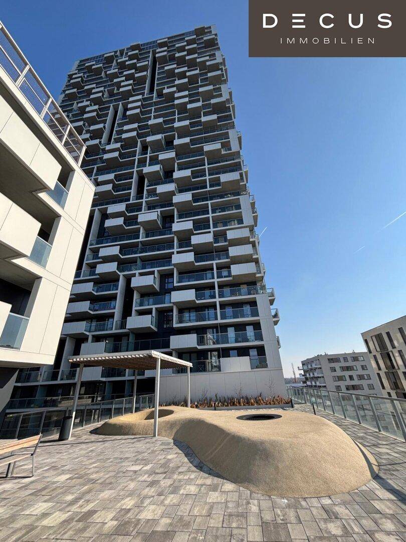 Große gepflasterte Terrasse mit Sitzgelegenheiten und Blick auf ein modernes Hochhaus.