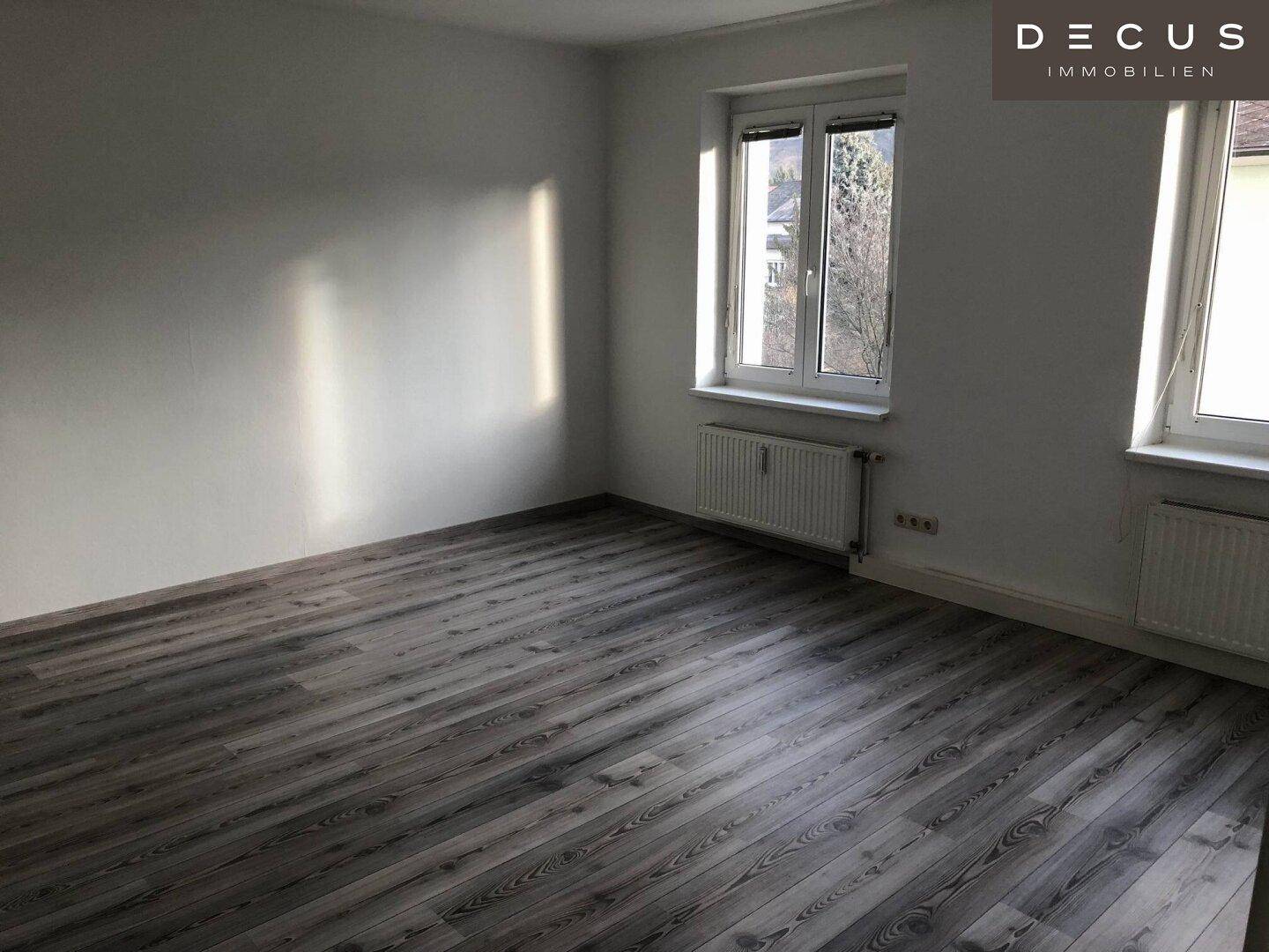 Helles Zimmer mit modernem Laminatboden und Heizkörper unter dem Fenster.