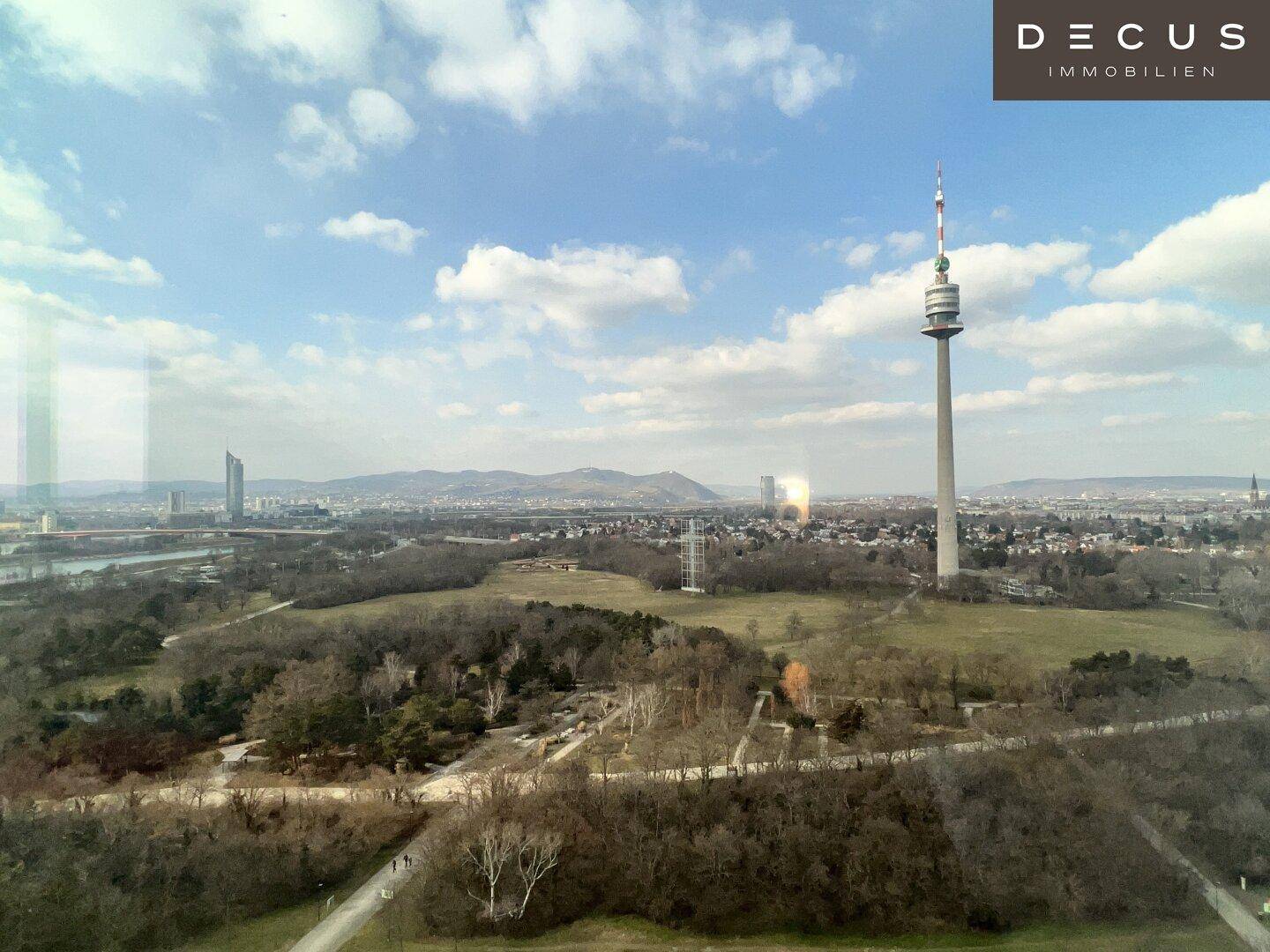 Panoramablick auf den Donauturm und die grüne Landschaft unter einem bewölkten Himmel.