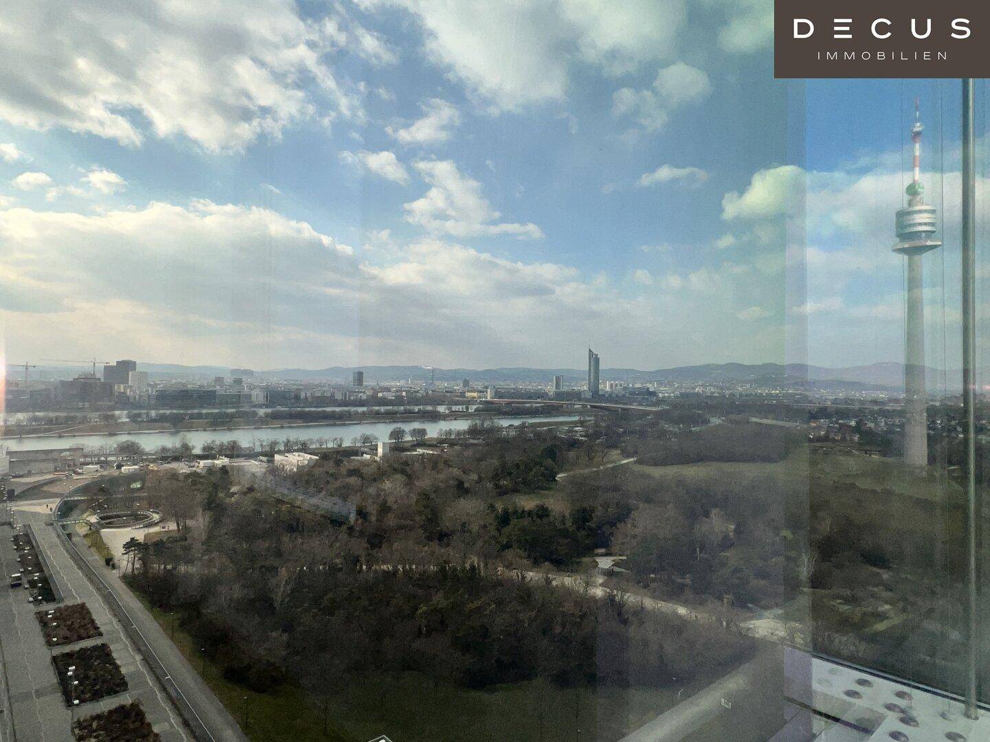 Weitläufiger Blick über die Donau, die Stadt und den Donauturm an einem sonnigen Tag.