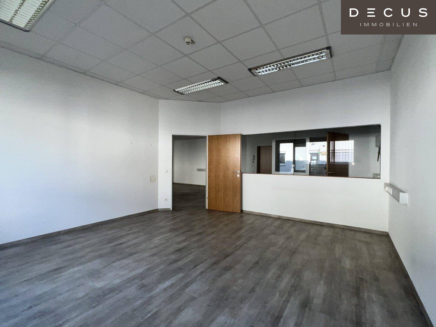 Leerer Bürobereich mit modernem Laminatboden und einer Holztür, die zu weiteren Räumen führt.