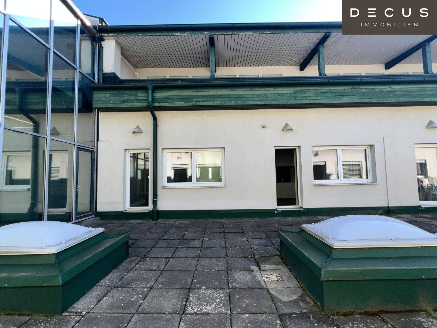 Große gepflasterte Terrasse mit Oberlichtern und Zugang zu den Innenräumen des Gebäudes.