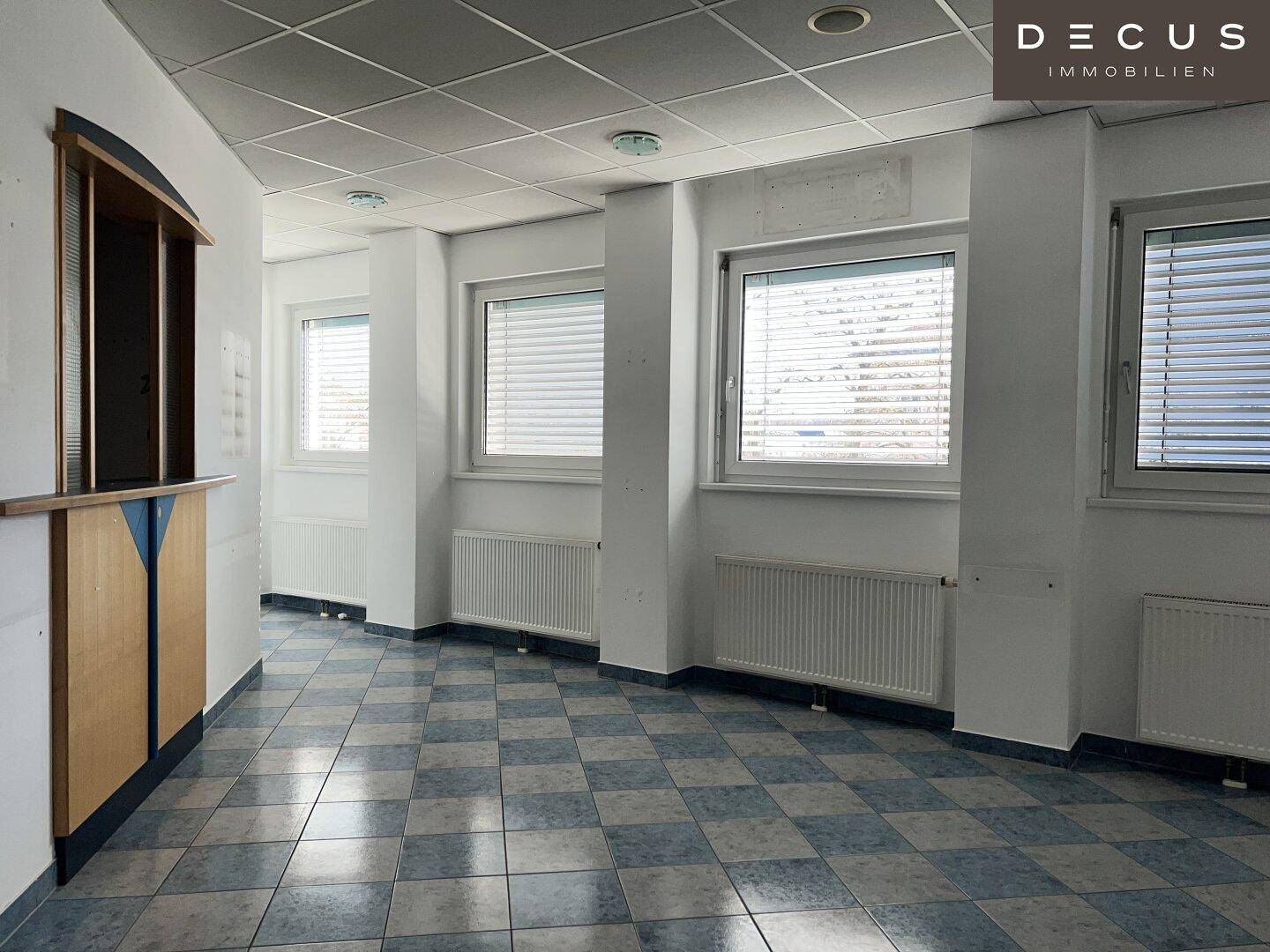 Heller Bürobereich mit mehreren Fenstern, Heizkörpern und einem charakteristischen Fliesenboden.