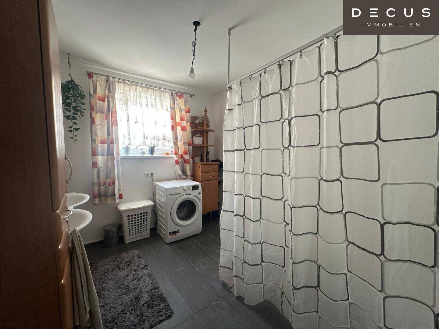 Badezimmer mit Dusche, Waschmaschine und Fenster für Tageslicht.