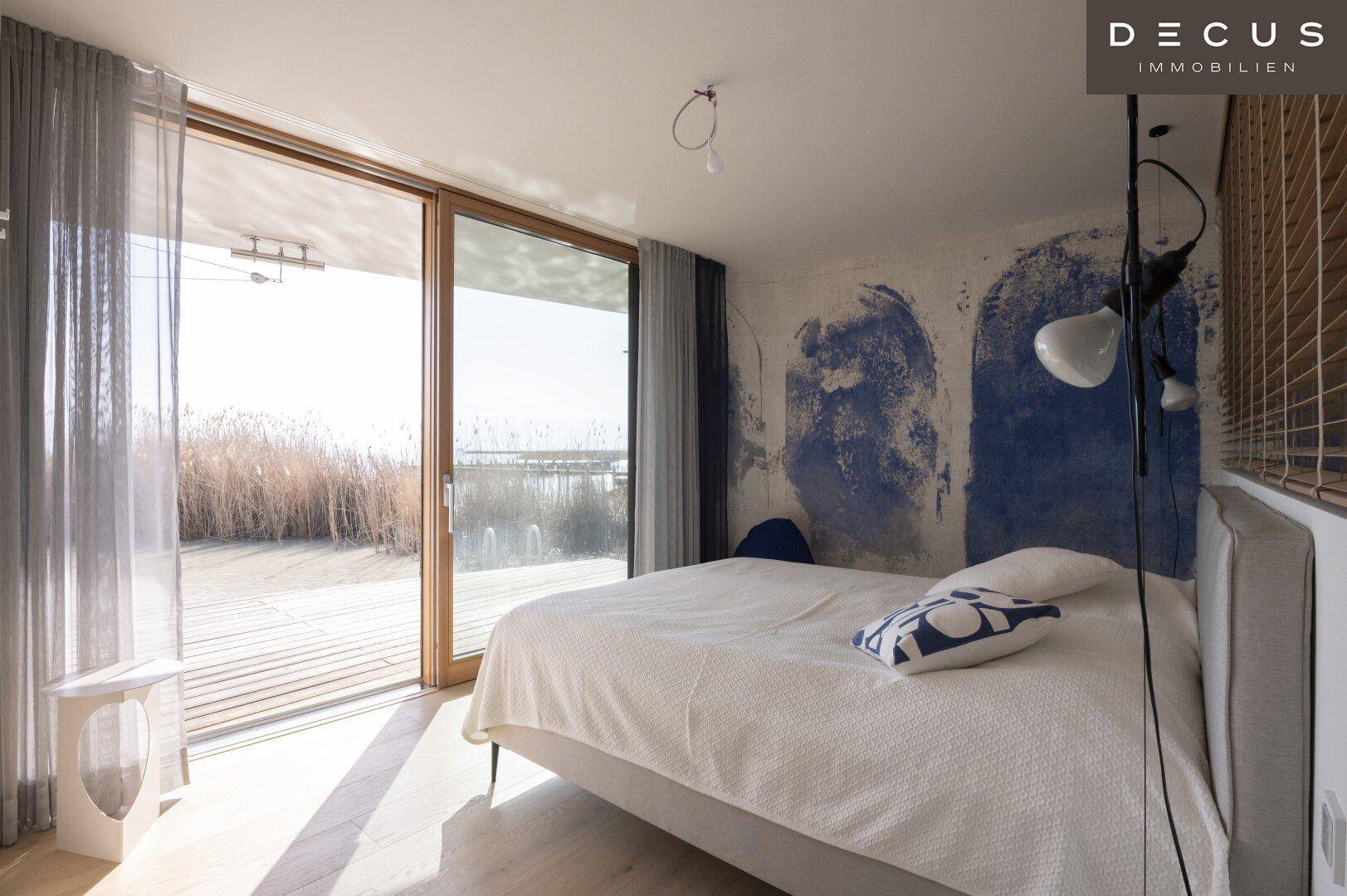 Helles Schlafzimmer mit großem Bett, blauer Wandgestaltung und direktem Terrassenzugang.