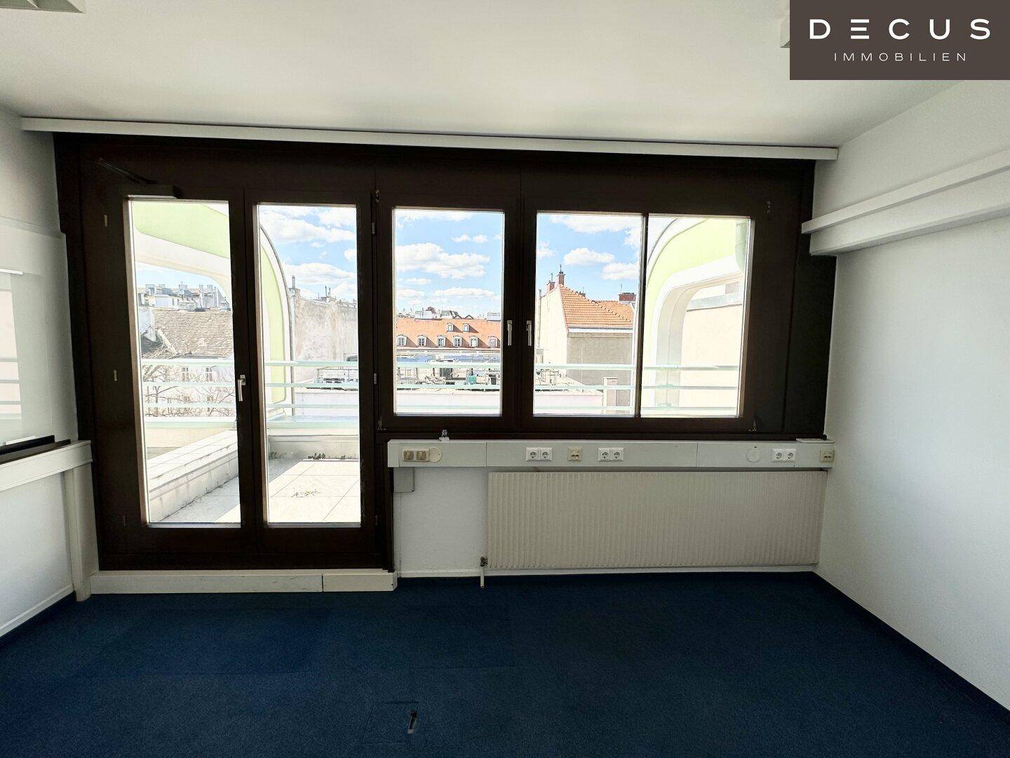Büroraum mit blauem Teppichboden und Zugang zu einer Terrasse, bietet viel natürliches Licht.