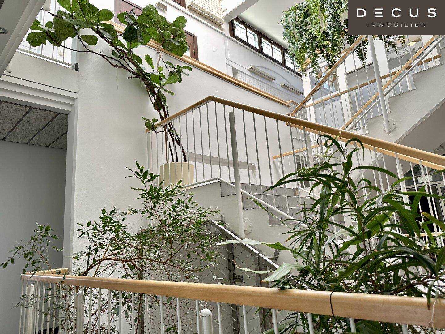 Treppenhaus mit Holzgeländer, Metallgittern und Pflanzen, verbindet verschiedene Ebenen des Gebäudes.