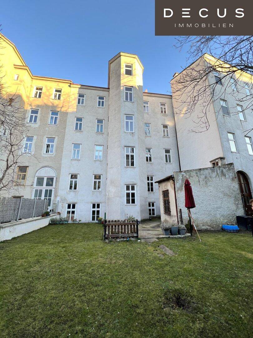 Hinterhofansicht eines historischen Gebäudes mit Rasenfläche und einem markanten Turm bei Sonnenuntergang.