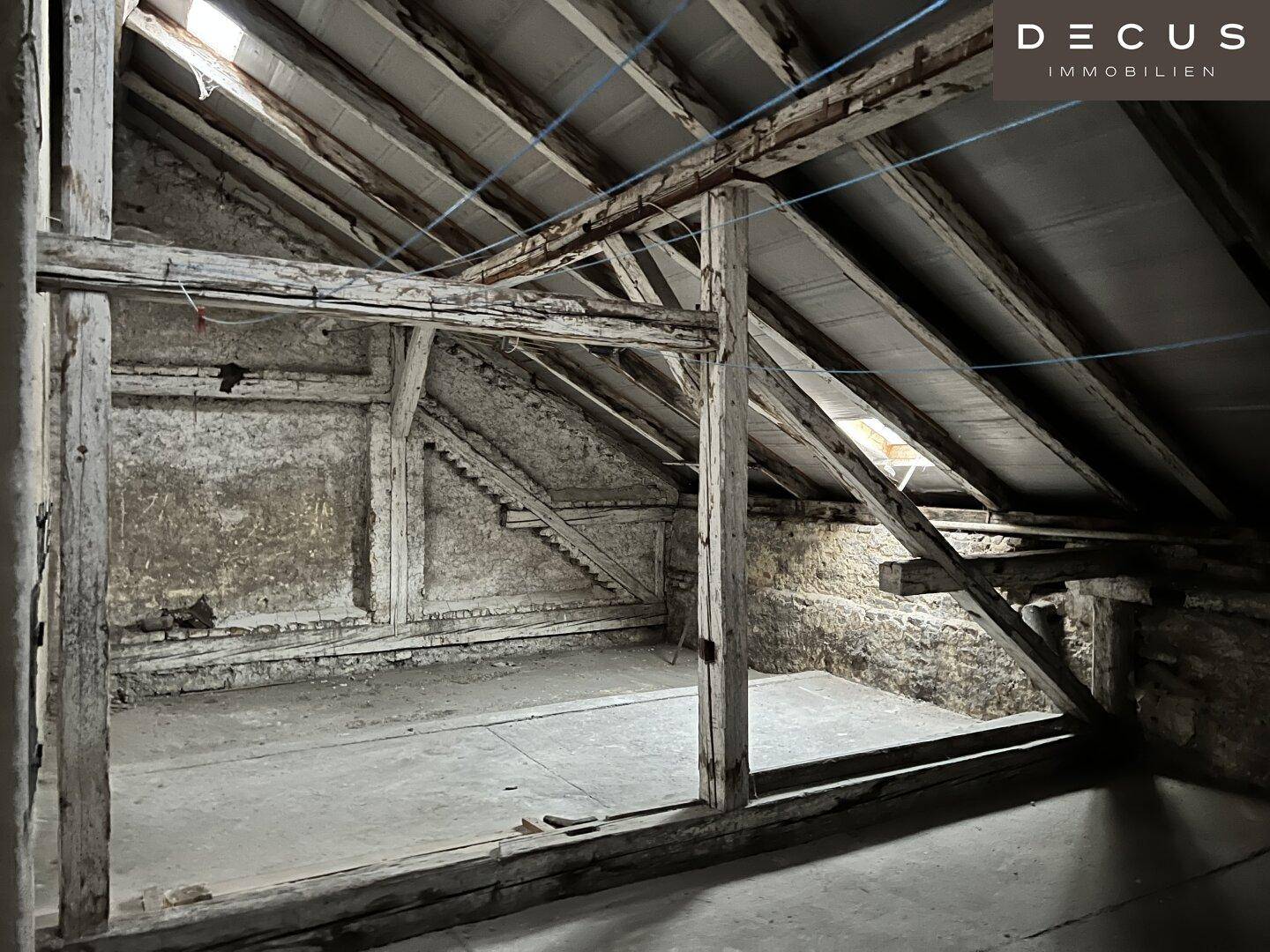 Unausgebauter Dachboden mit sichtbaren Holzbalken und rauen Wänden, bereit für den Ausbau.