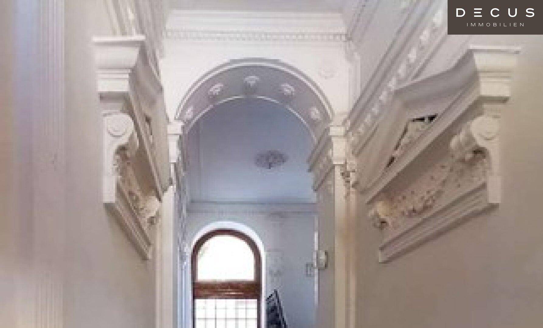 Prächtiger Flur mit aufwendigen Stuckverzierungen an Wänden und Decke sowie einem Rundbogenfenster.