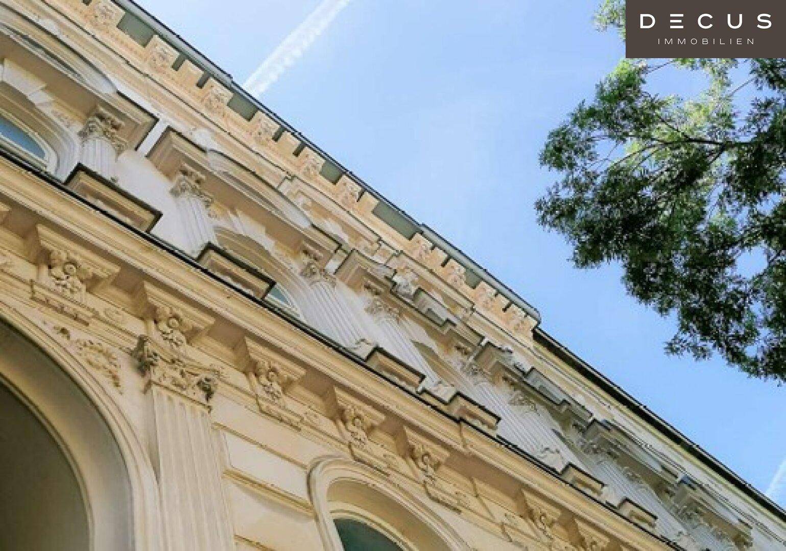 Detailansicht der reich verzierten Fassade eines Altbaus mit Stuckelementen unter blauem Himmel.