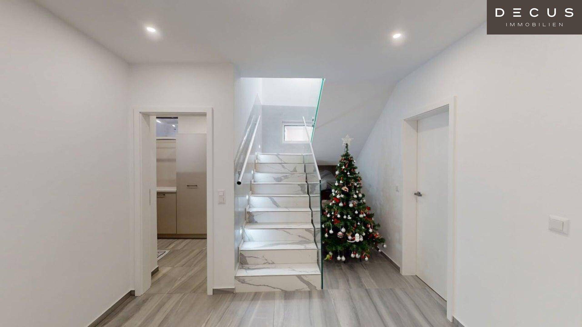 Heller Eingangsbereich mit moderner Treppe, Weihnachtsbaum und Zugang zu weiteren Räumen.