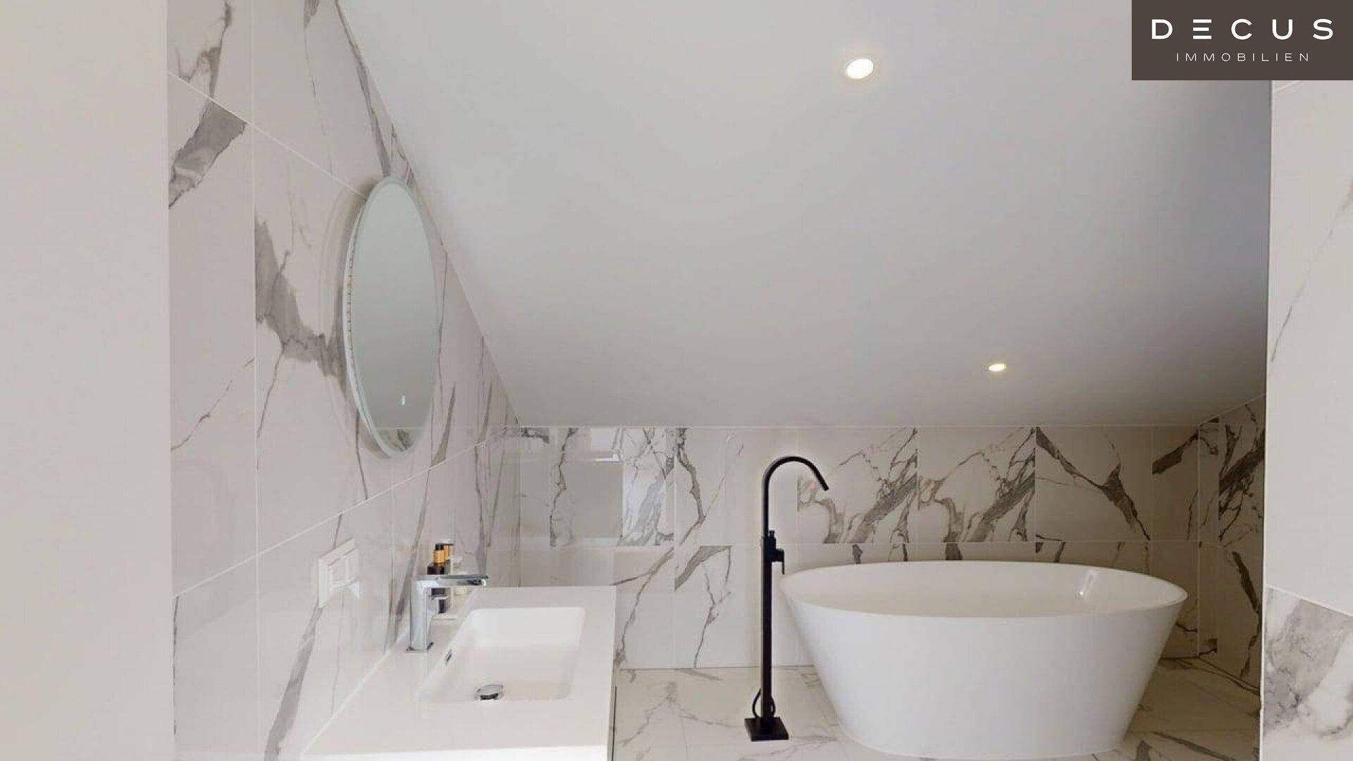 Elegantes Badezimmer im Dachgeschoss mit freistehender Badewanne und Marmorfliesen.