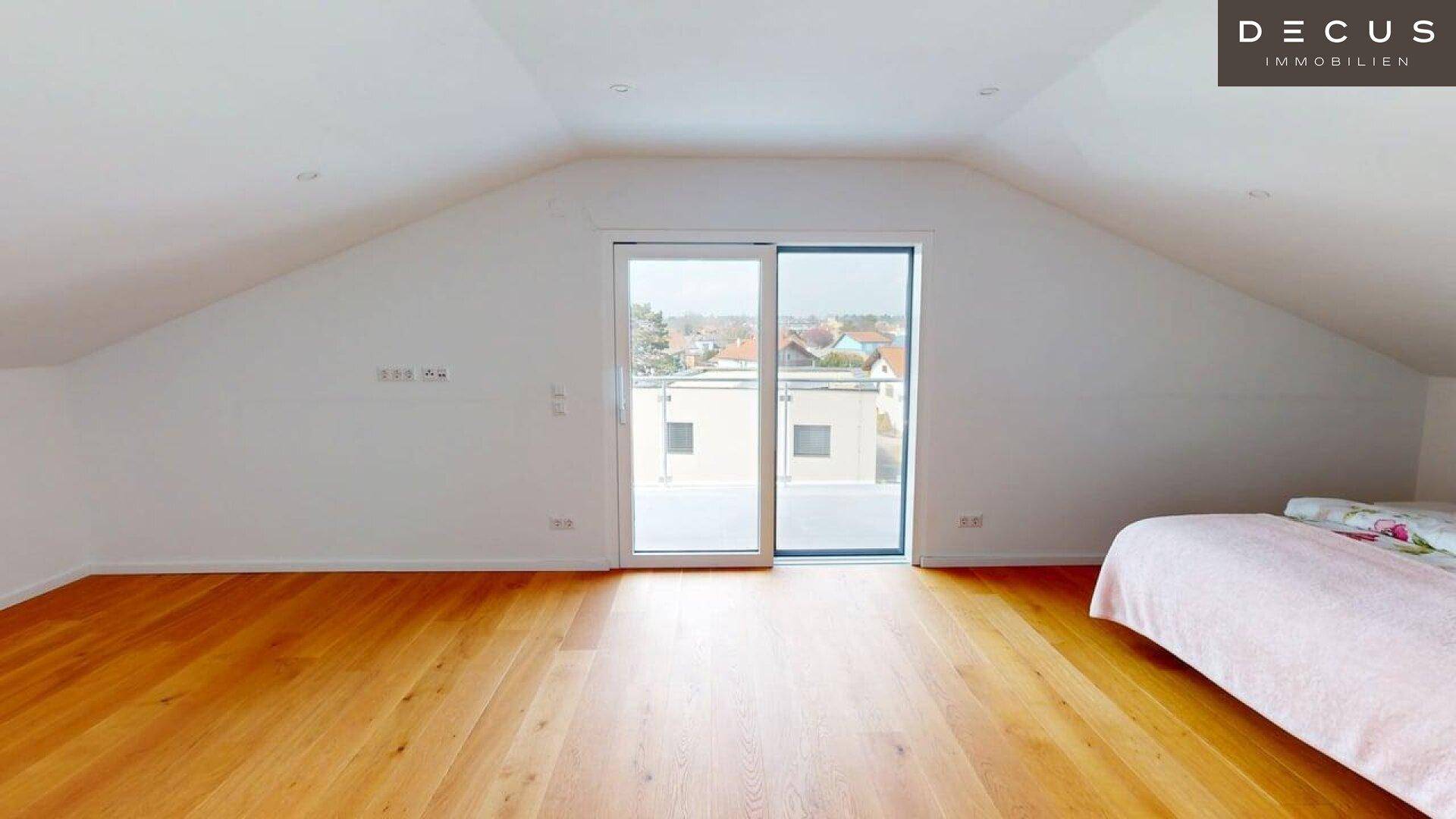 Geräumiges Schlafzimmer im Dachgeschoss mit Holzboden und Zugang zu einem Außenbereich.
