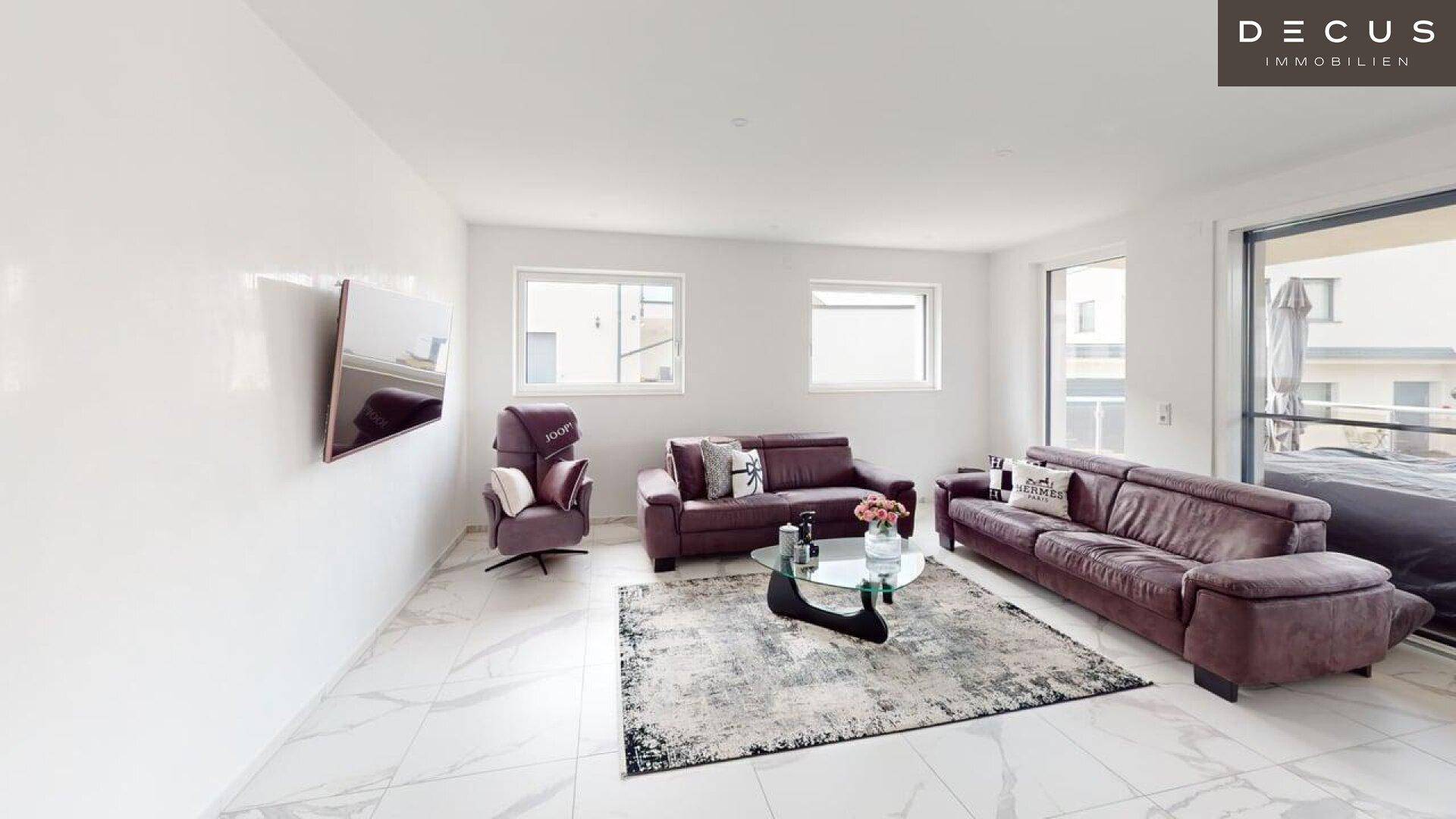 Gemütliches Wohnzimmer mit bequemen Sofas, modernem Teppich und großen Fenstern.