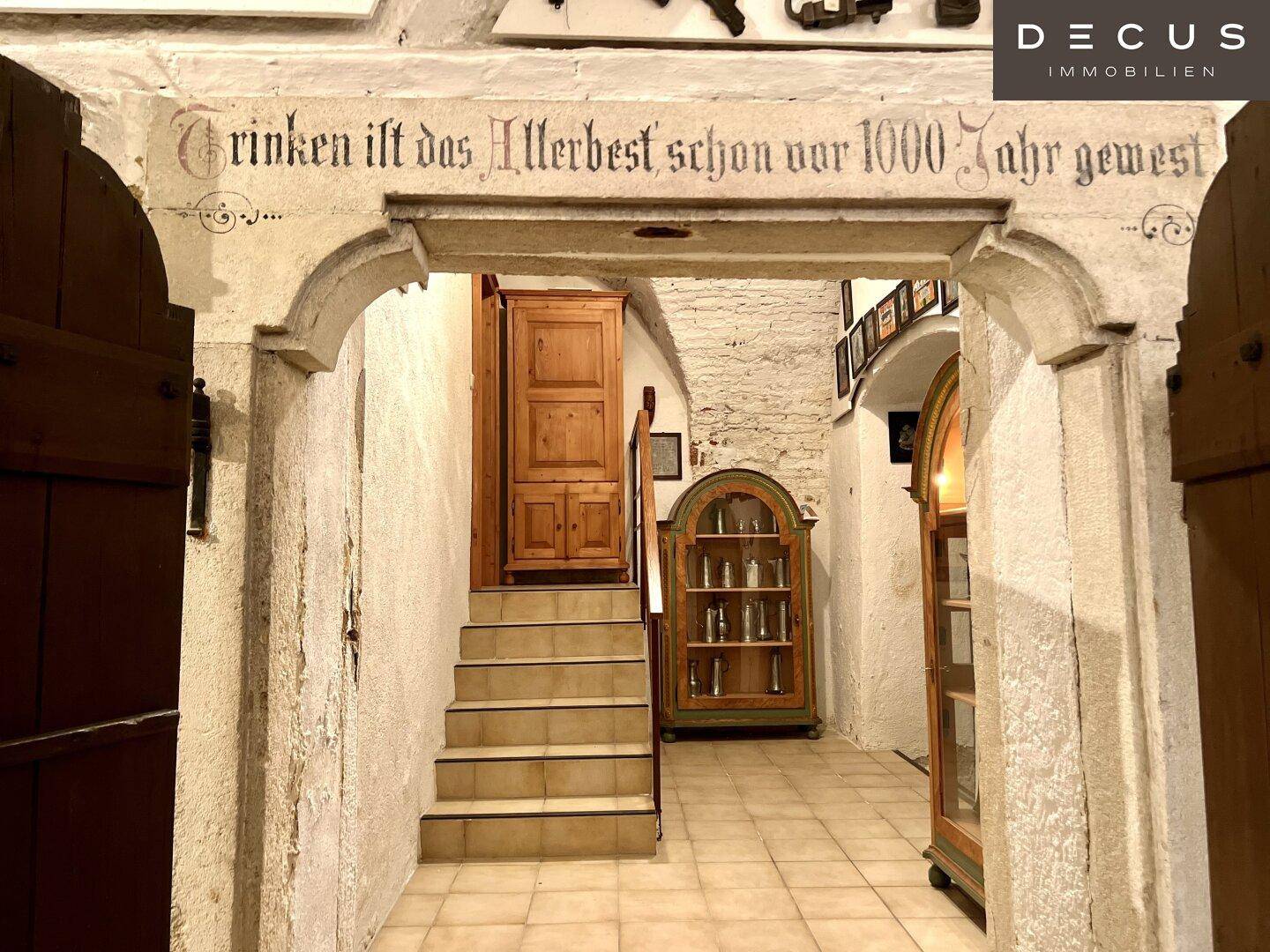 Historischer Durchgang mit Steinbogen, Treppe und antiken Möbeln, verziert mit alter Schrift.
