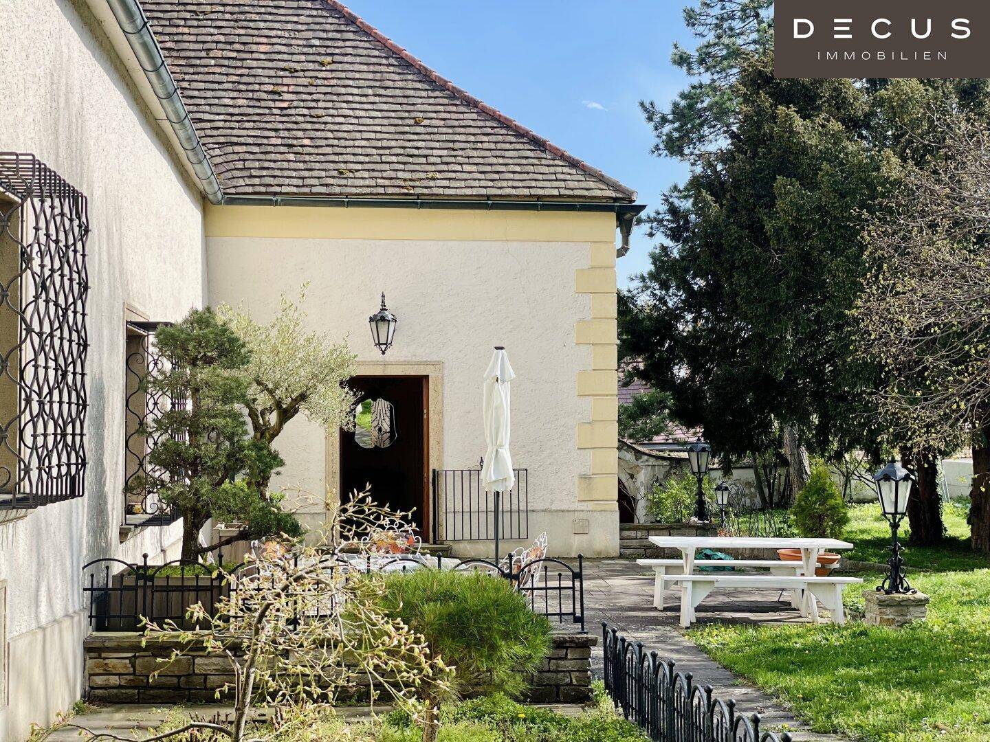 Gepflegter Gartenbereich mit weißer Picknickbank und historischer Hausfassade unter blauem Himmel.