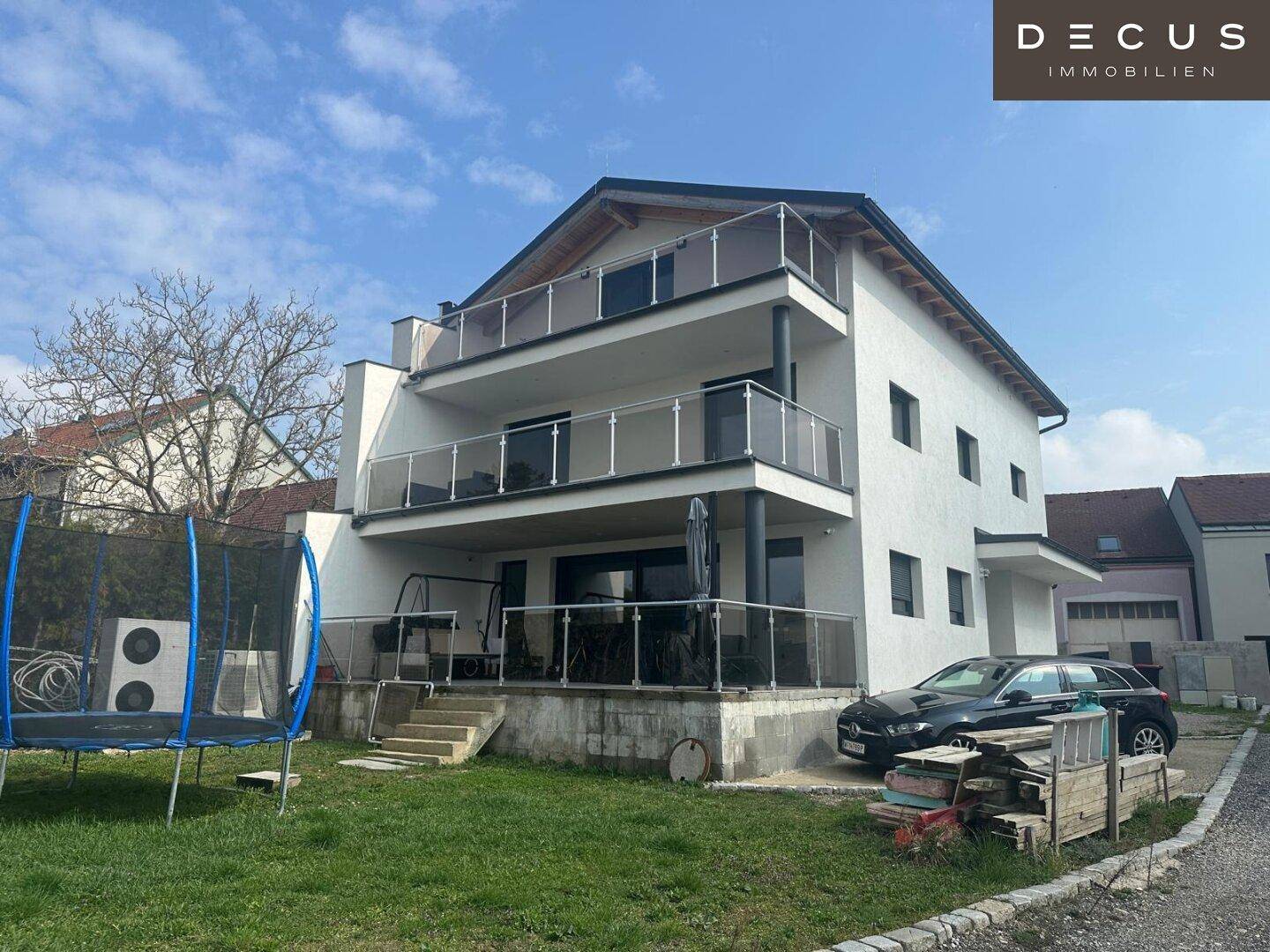 Modernes weißes Gebäude mit mehreren Balkonen und einem Gartenbereich mit Trampolin.