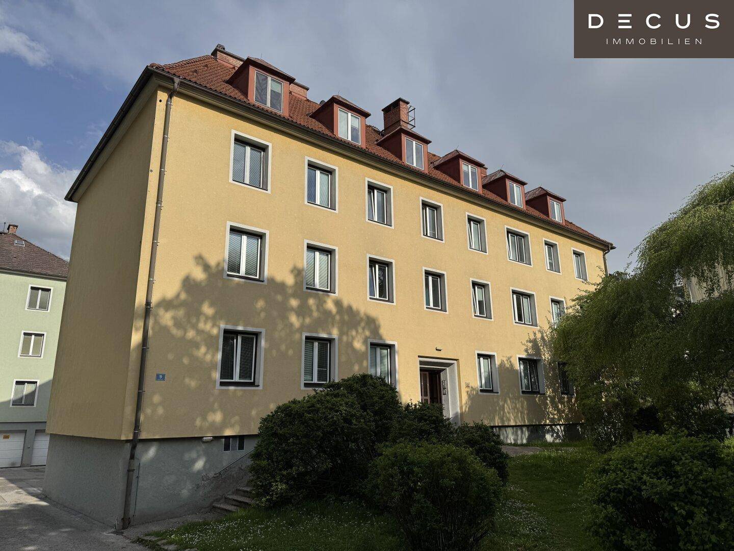 Gelbes Mehrfamilienhaus mit rotem Ziegeldach und vielen Fenstern unter blauem Himmel.