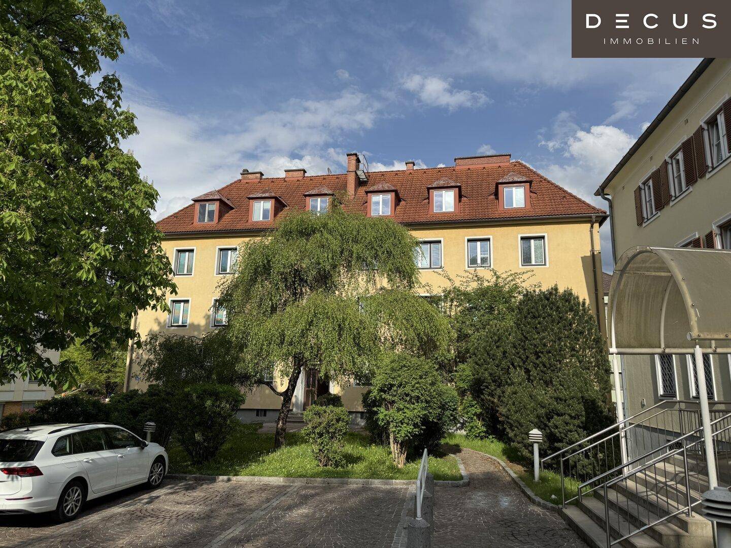 Eingangsbereich eines gelben Mehrfamilienhauses mit Bäumen und gepflegter Außenanlage.
