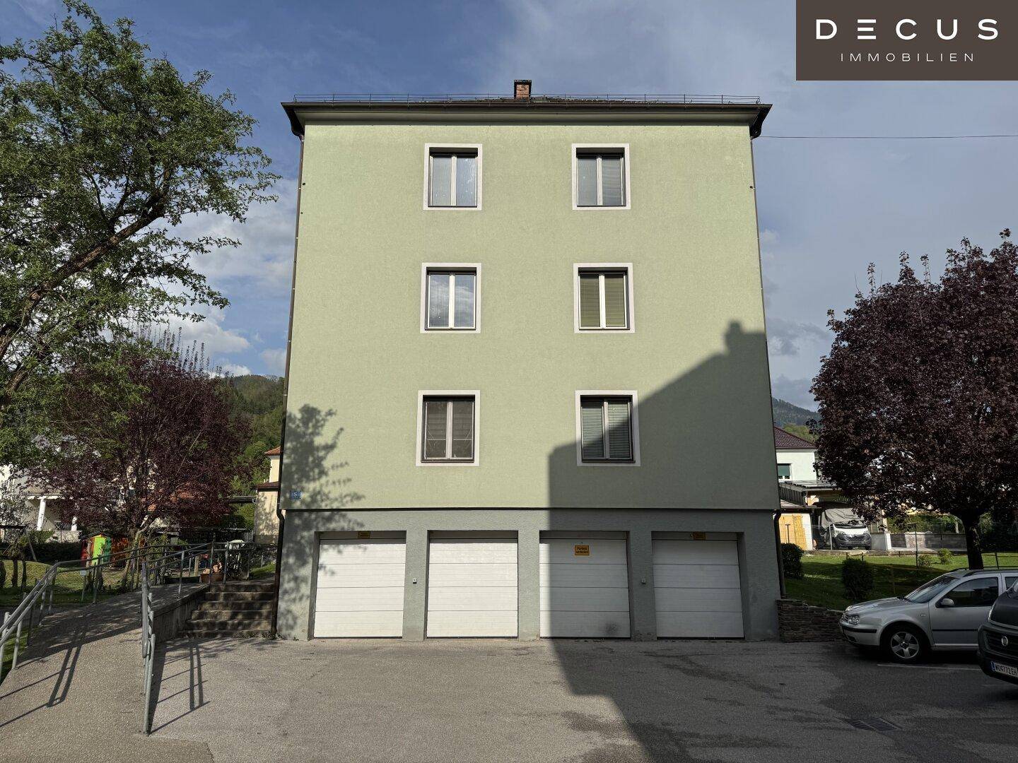 Rückseite eines Mehrfamilienhauses mit Garagen im Erdgeschoss und grüner Fassade.