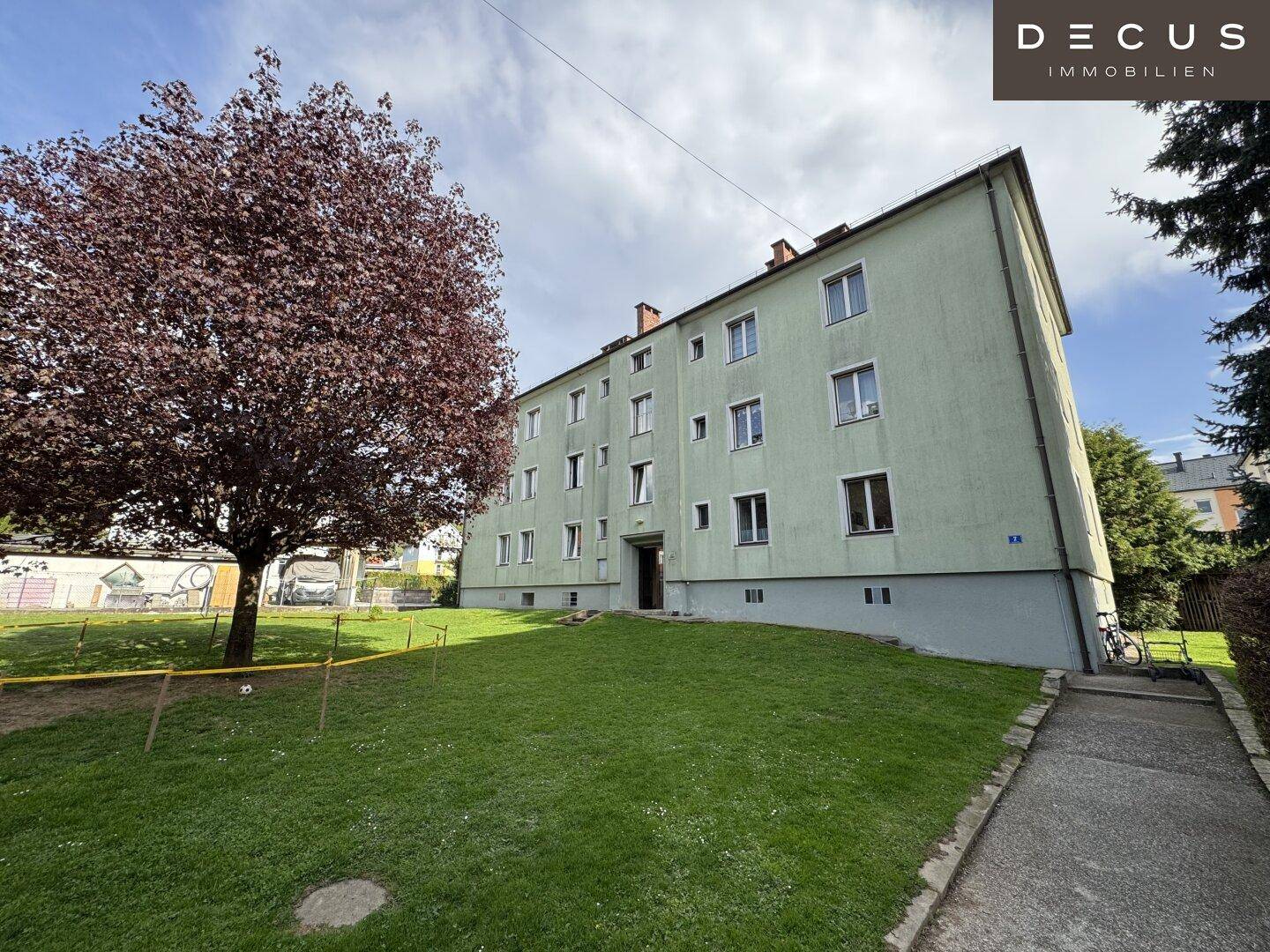 Gepflegter Gemeinschaftsgarten mit Rasenfläche und altem Baum vor dem Wohngebäude.