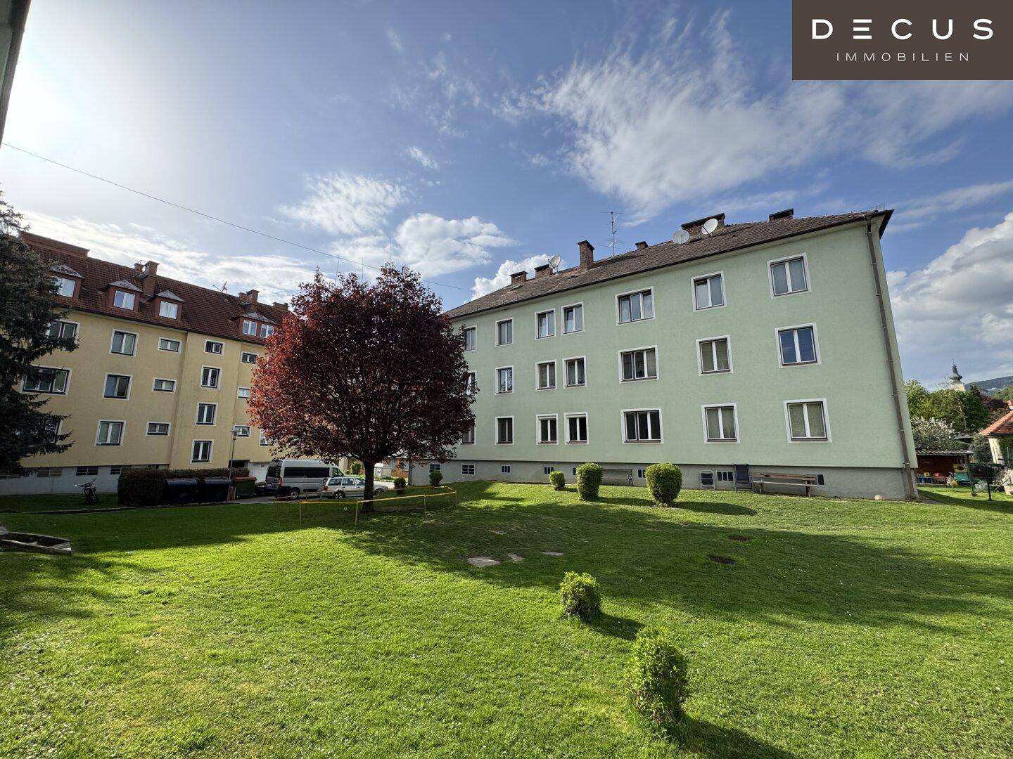 Gemeinschaftlicher Gartenbereich mit Rasenfläche und Bäumen zwischen zwei Mehrfamilienhäusern.