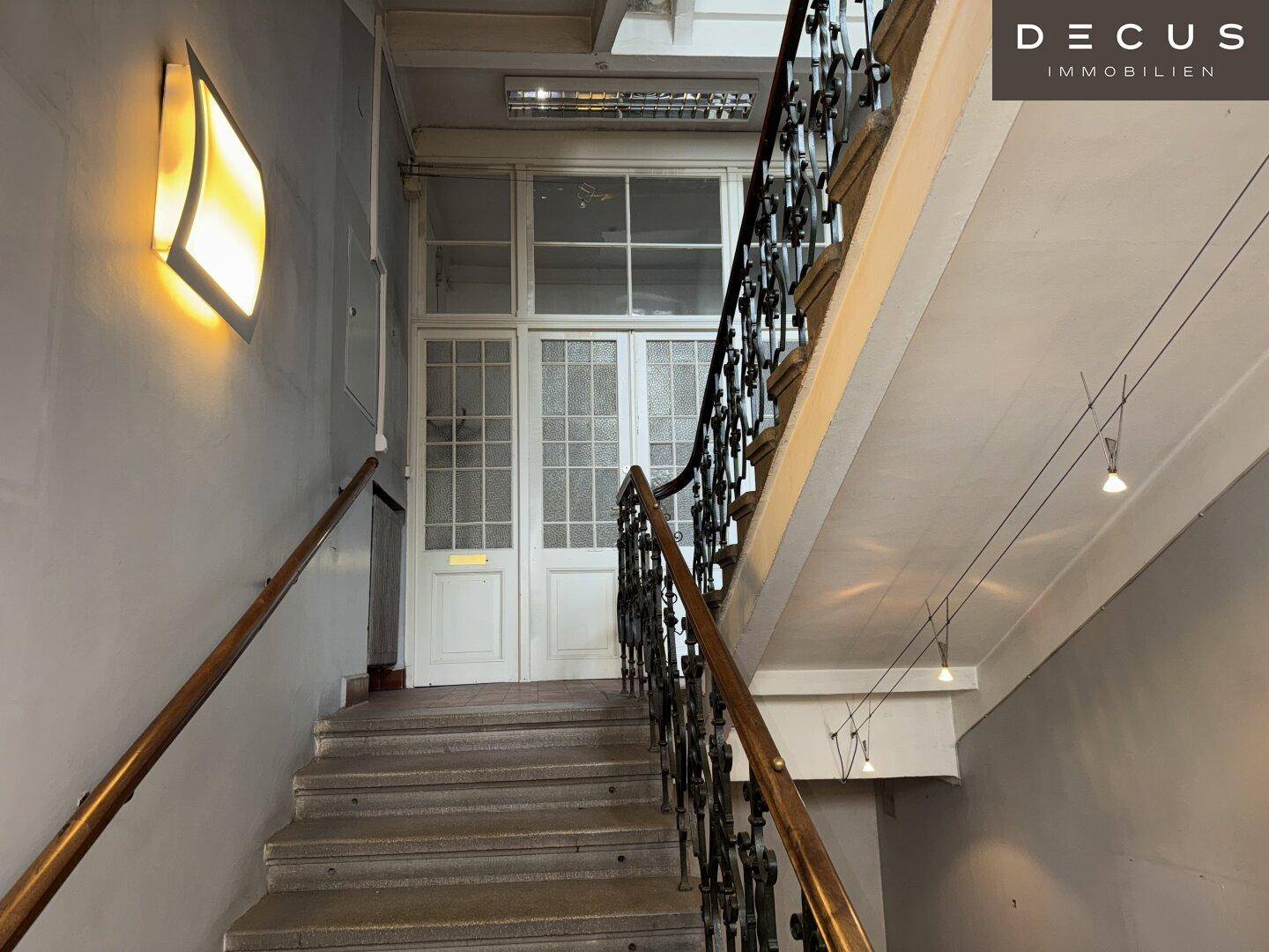 Historisches Treppenhaus mit schmiedeeisernem Geländer und hohen Decken in einem Altbau.