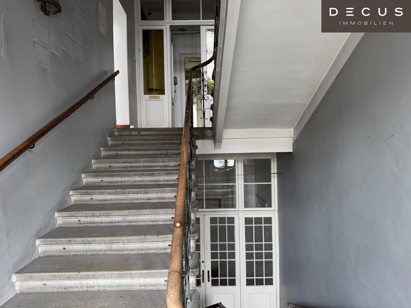 Eingangsbereich mit Treppenaufgang, hohen Decken und historischen Türen in einem Altbau.