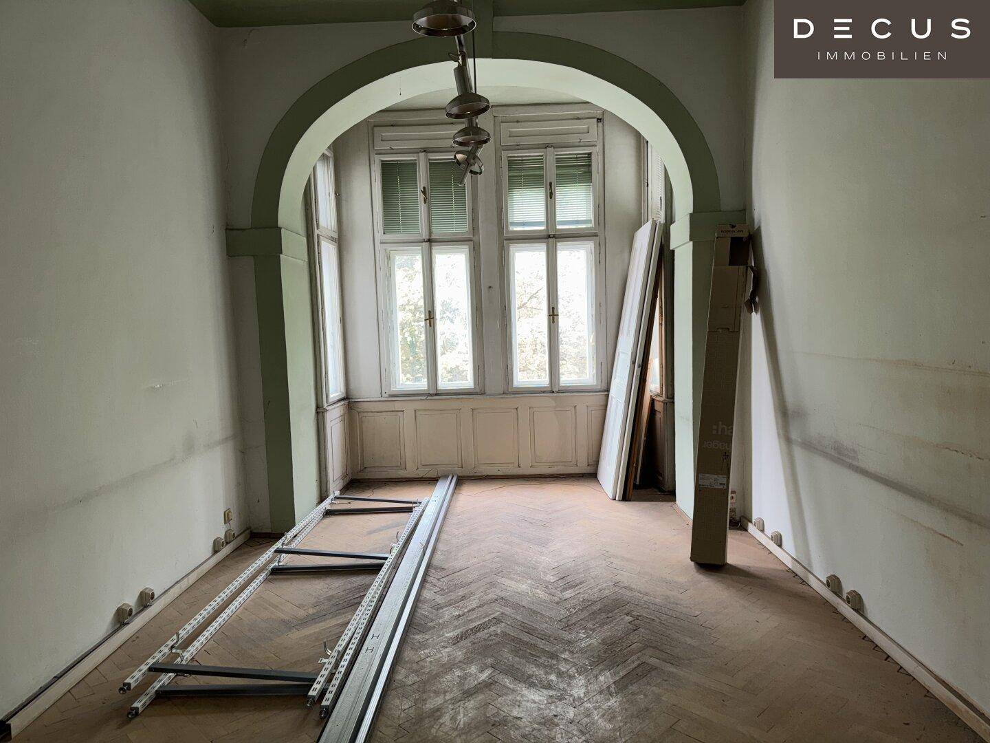 Geräumiger Altbau-Raum mit Fischgrätparkett, hohen Fenstern und Renovierungsbedarf.