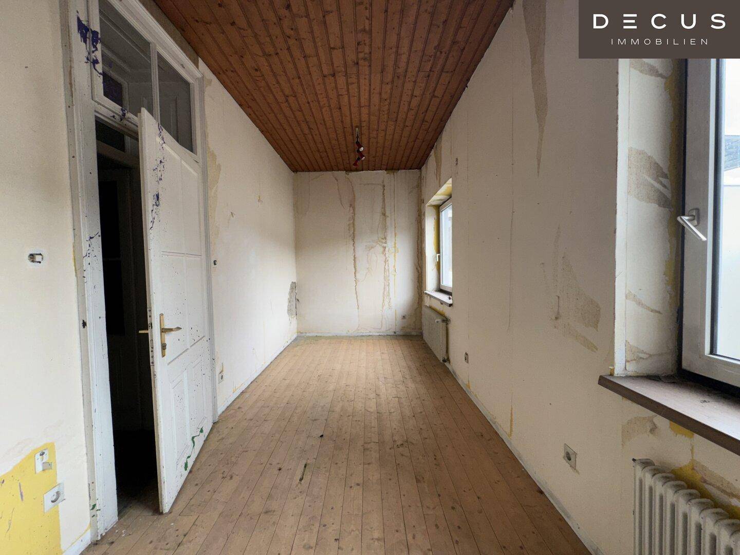 Kleiner Raum mit Holzdielenboden, Holzdecke und Renovierungsbedarf in einem Altbau.
