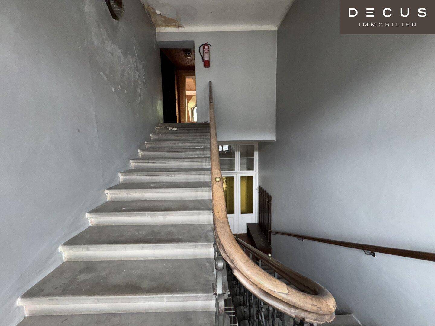 Treppenhaus mit Steinstufen, Holzgeländer und Brandschutzvorrichtung in einem Altbau.
