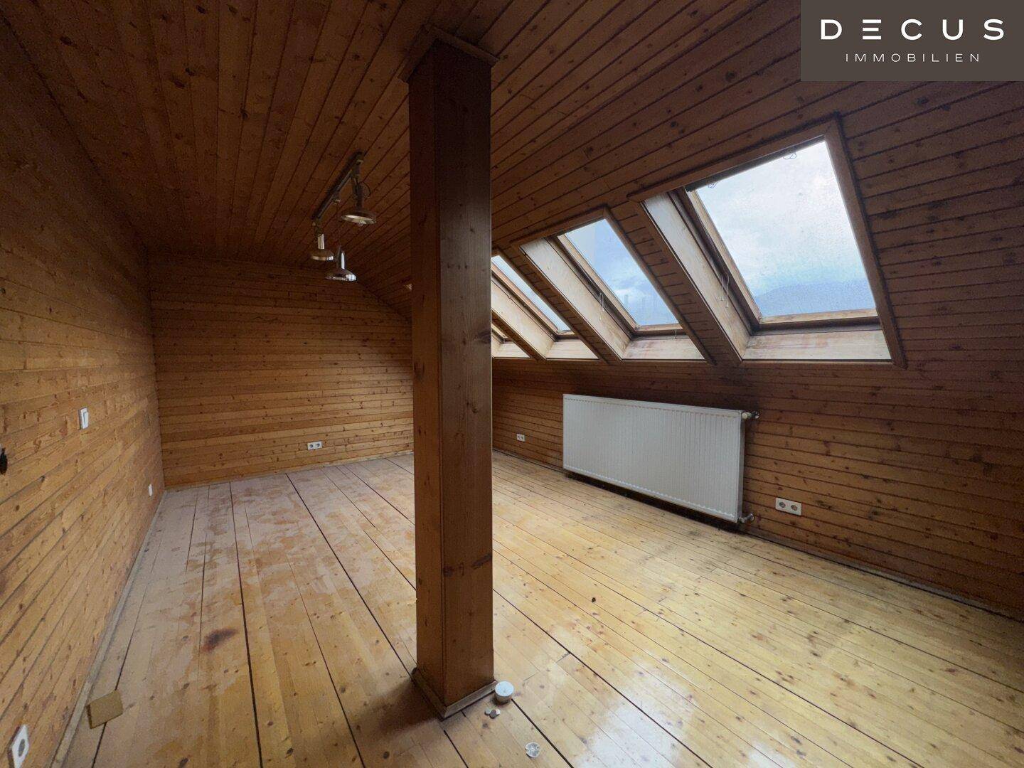 Ausgebauter Dachbodenraum mit Holzverkleidung, Holzboden und mehreren Dachfenstern.