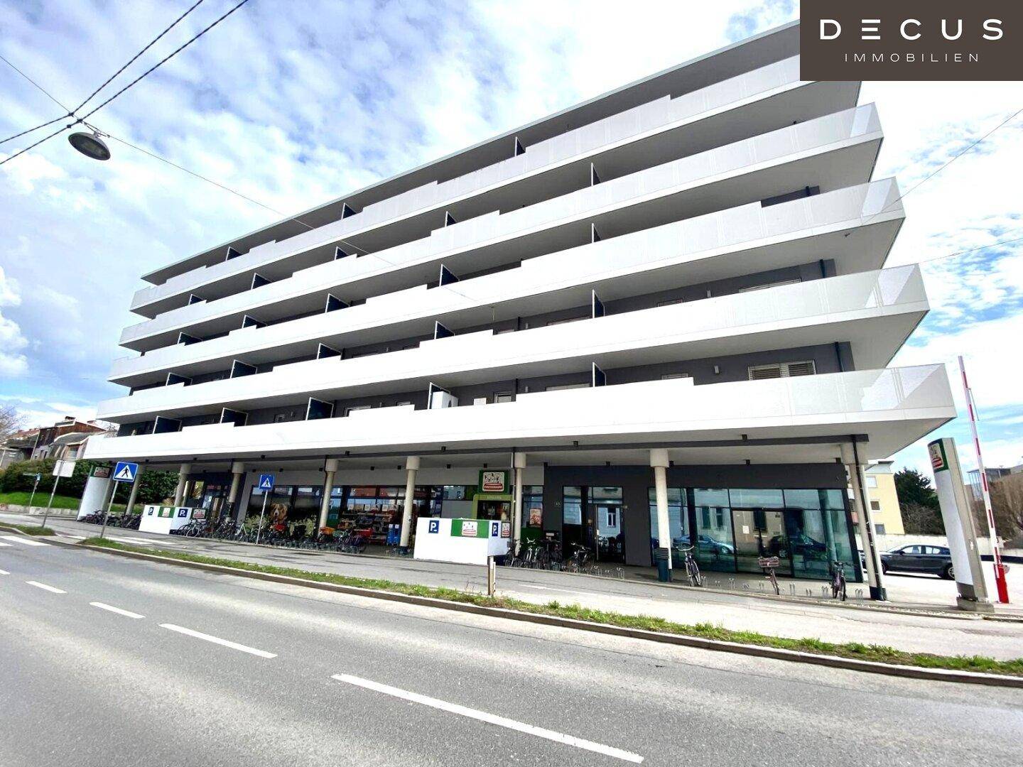 Modernes Mehrfamilienhaus mit mehreren Etagen, Balkonen und Geschäftsflächen im Erdgeschoss.