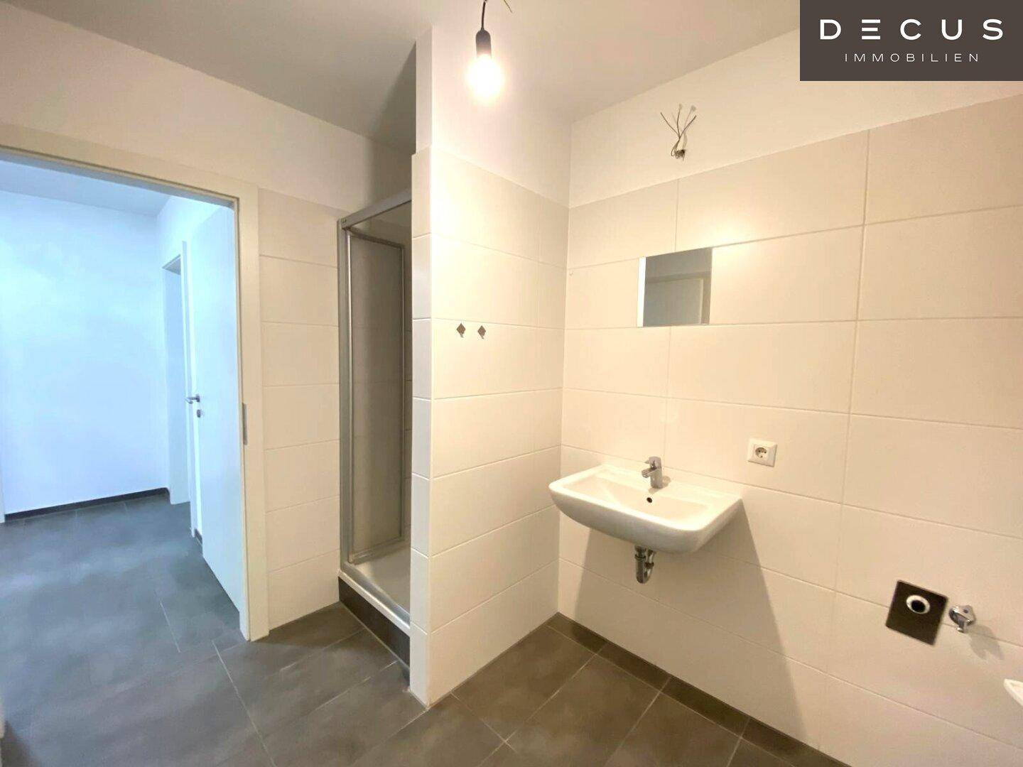 Funktionales Badezimmer mit weißen Wandfliesen, einer Duschkabine und einem einzelnen Waschbecken.