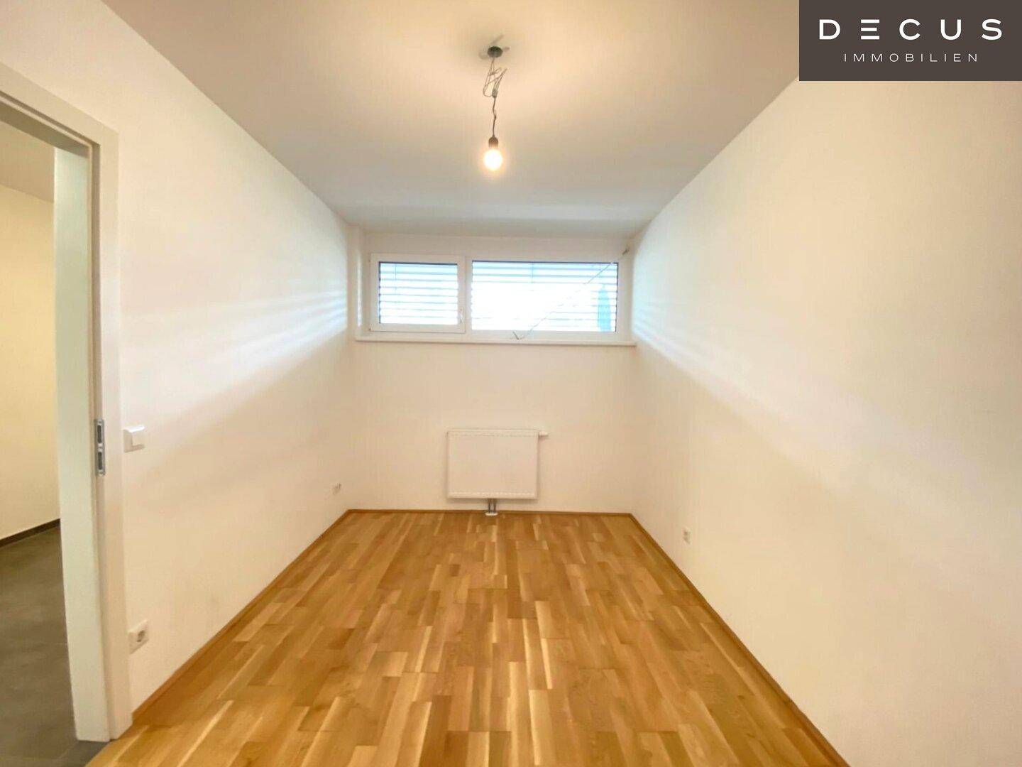 Leeres Schlafzimmer mit Holzboden und einem Fenster, das für natürliches Licht sorgt.