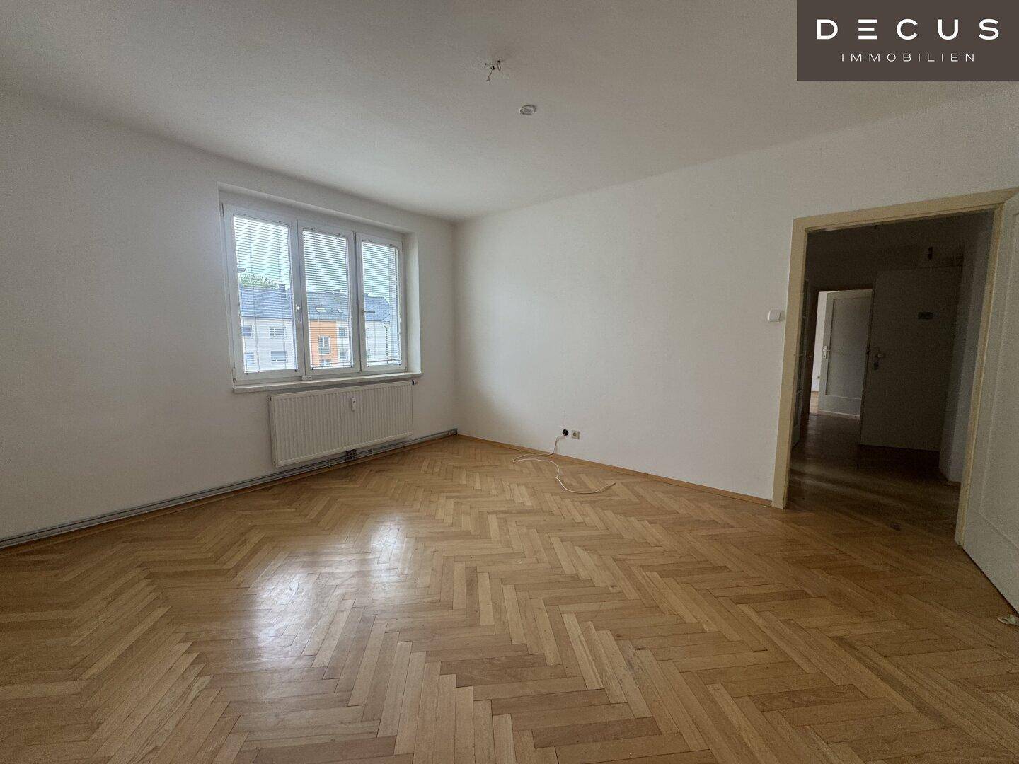 Helles Zimmer mit klassischem Fischgrätparkett und großem Fenster, gut erhalten.