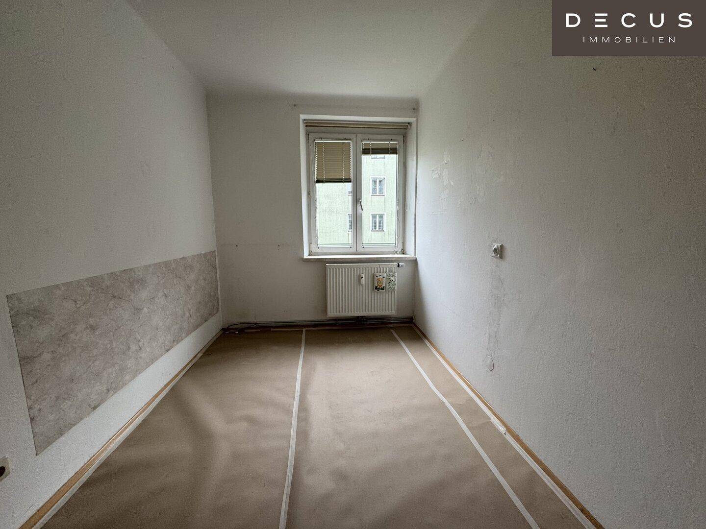 Zimmer in Renovierung mit vorbereitetem Boden und Fenster für natürliches Licht.