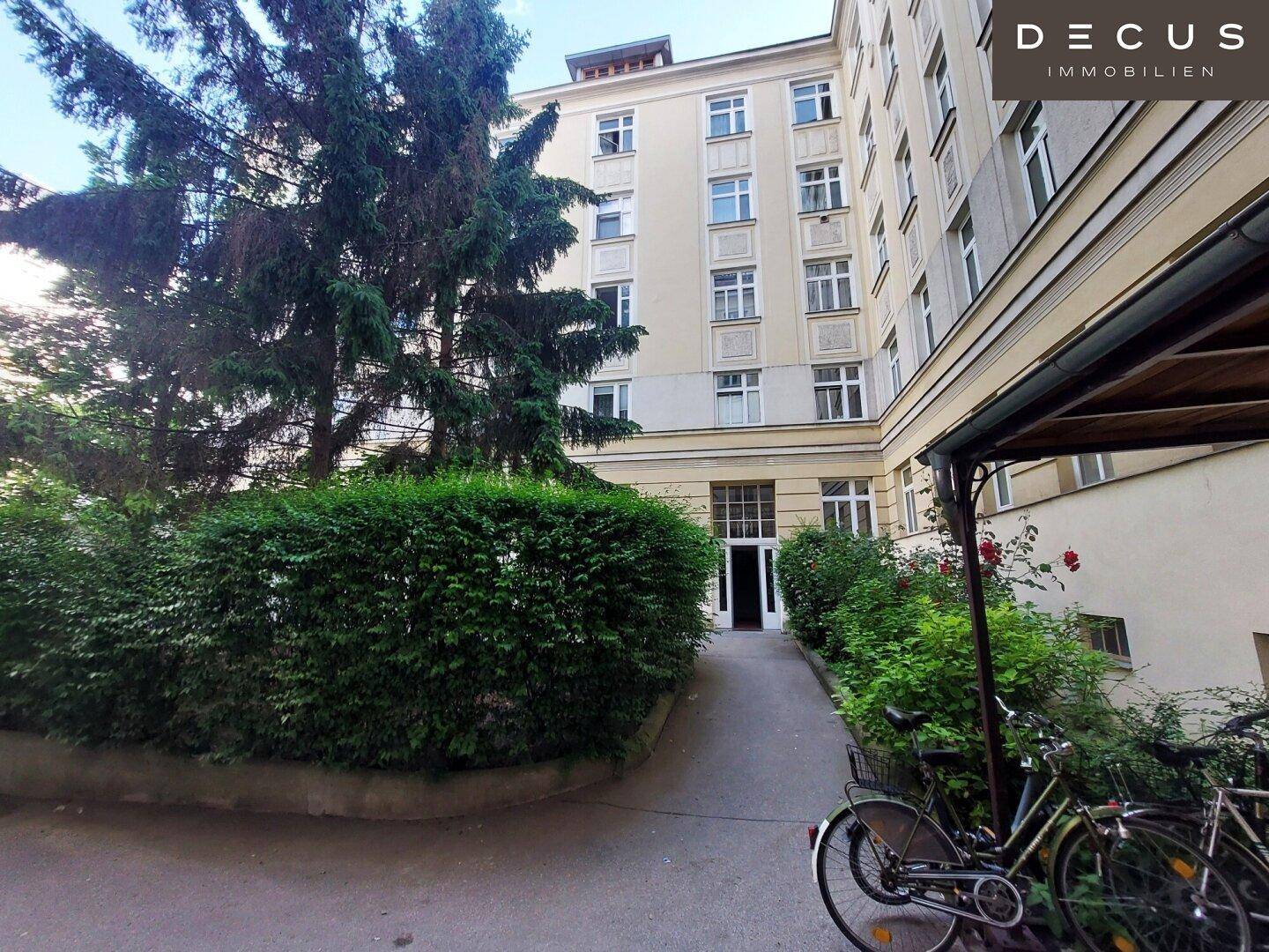 Historisches Mehrfamilienhaus mit gepflegter Fassade, grünem Innenhof und Fahrradabstellmöglichkeiten am Eingang.