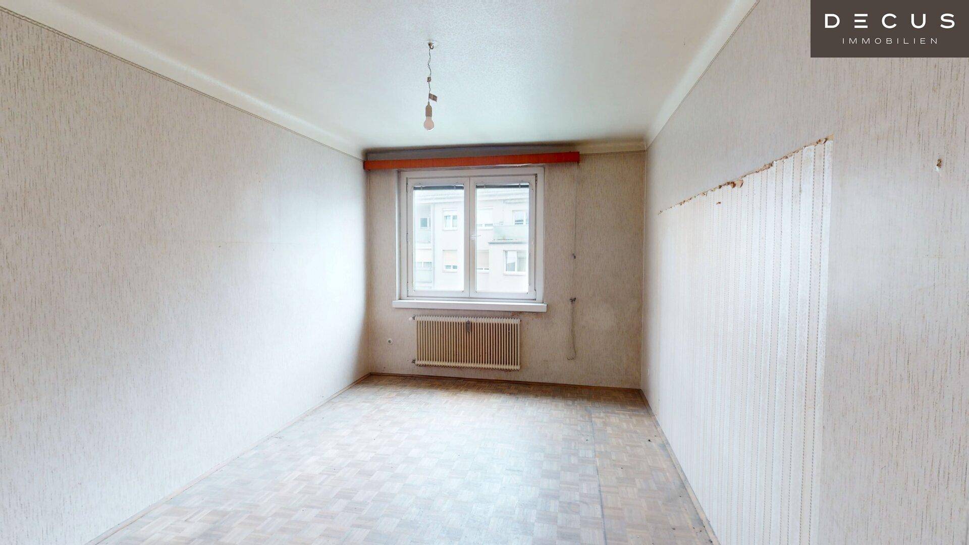 Leerer Raum mit gestreifter Tapete und Fenster, bereit für eine umfassende Renovierung.