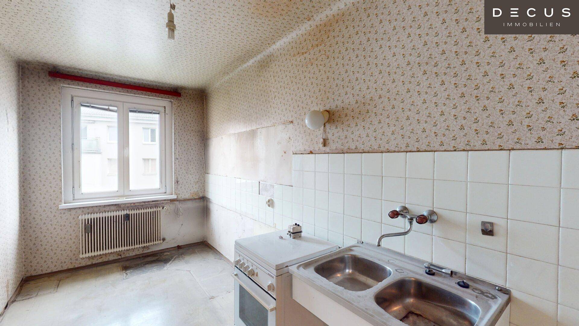 Küche mit älterer Ausstattung, Fliesen und floraler Tapete, ideal für eine Modernisierung.