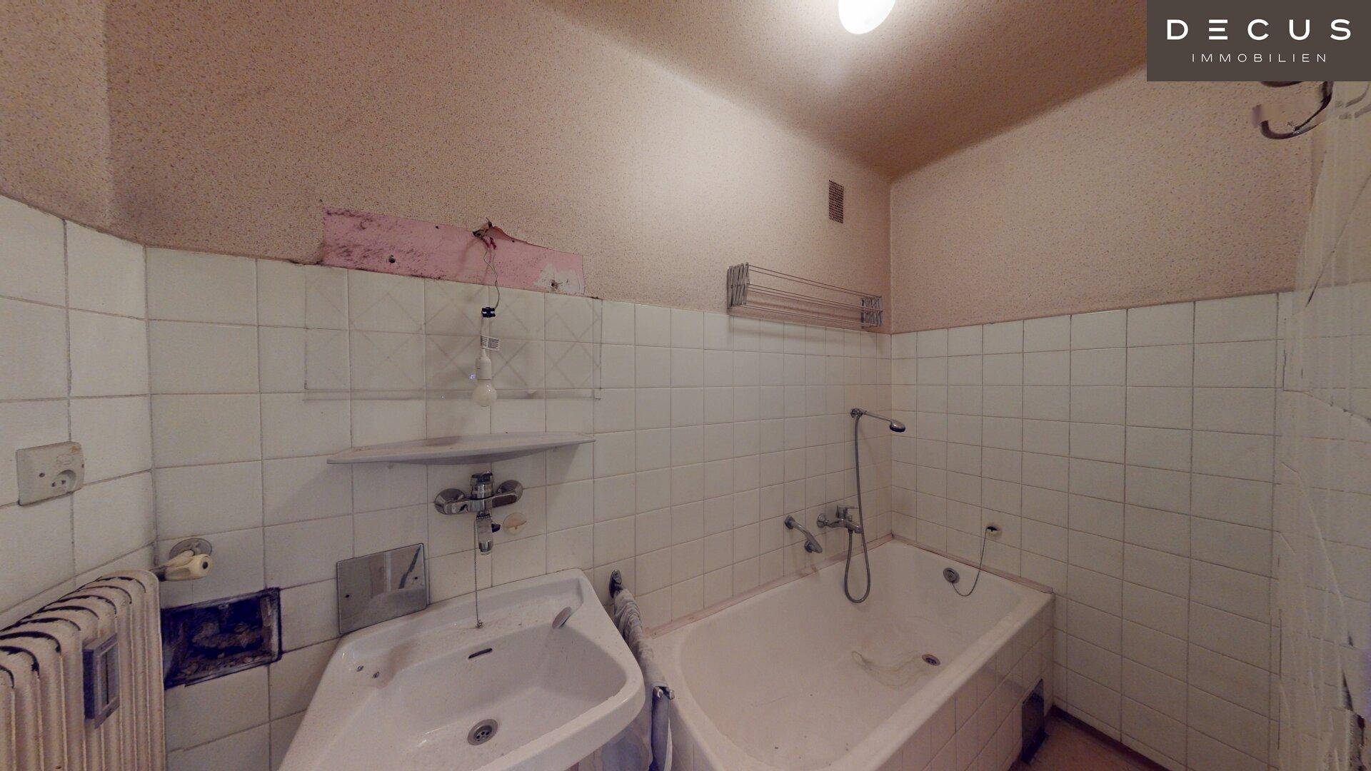 Badezimmer mit einfacher Ausstattung, weißen Fliesen und Badewanne, benötigt Modernisierung.