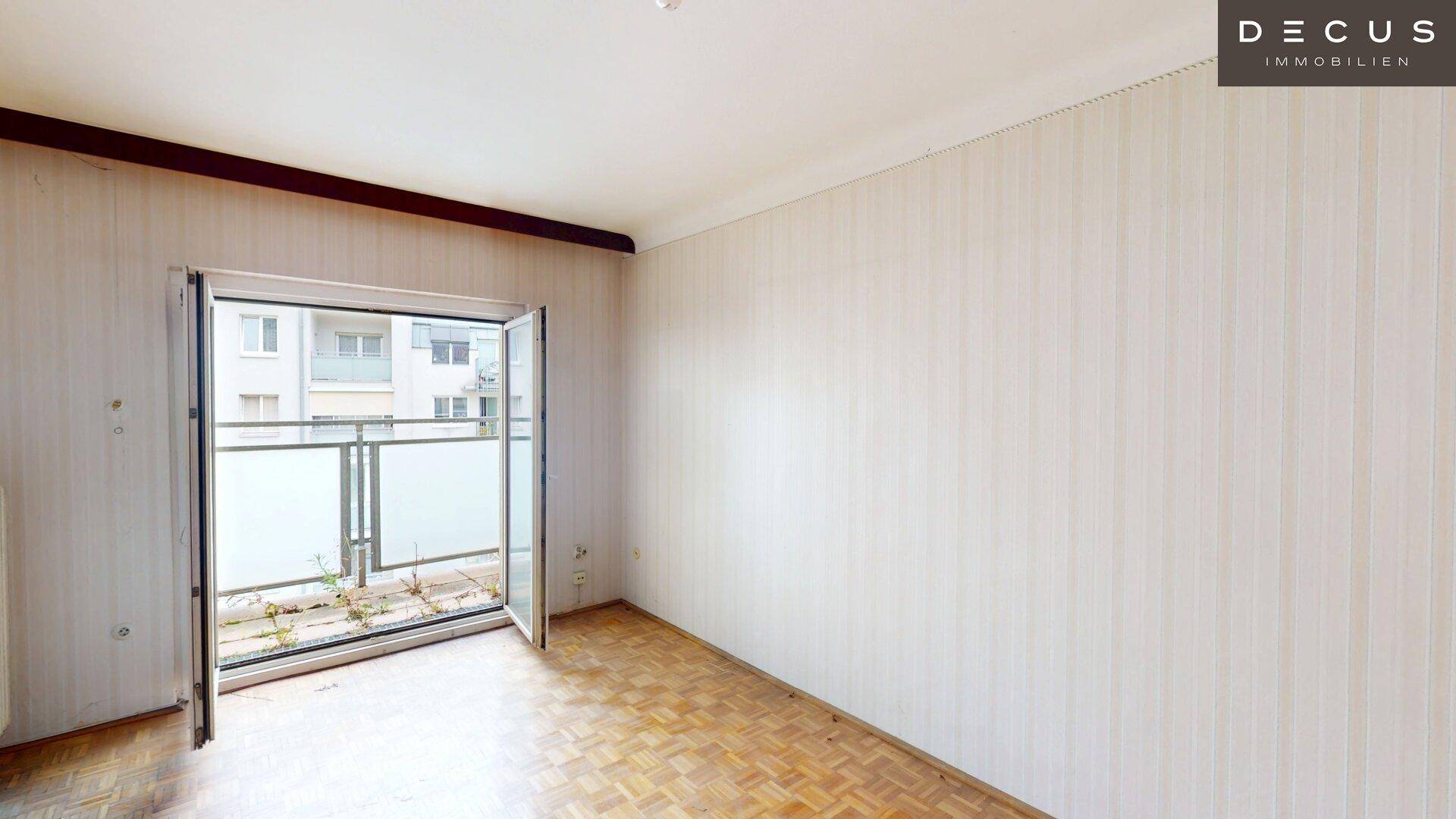 Leerer Wohnraum mit Fischgrätparkett und Zugang zu einem Balkon, bereit zur Renovierung.