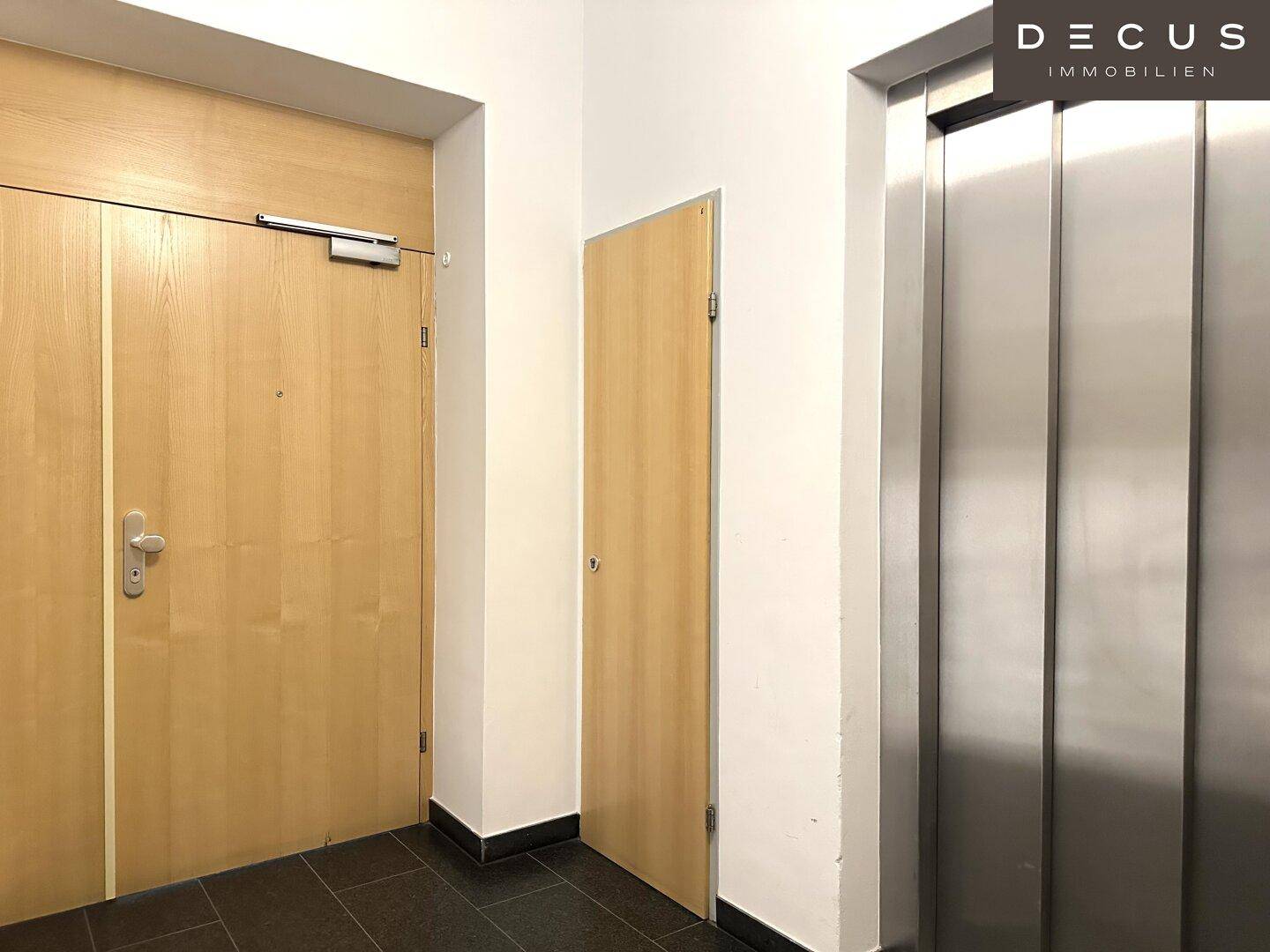 Moderner Eingangsbereich mit Holztüren und einem glänzenden Aufzug in Edelstahloptik, sauber und funktional.