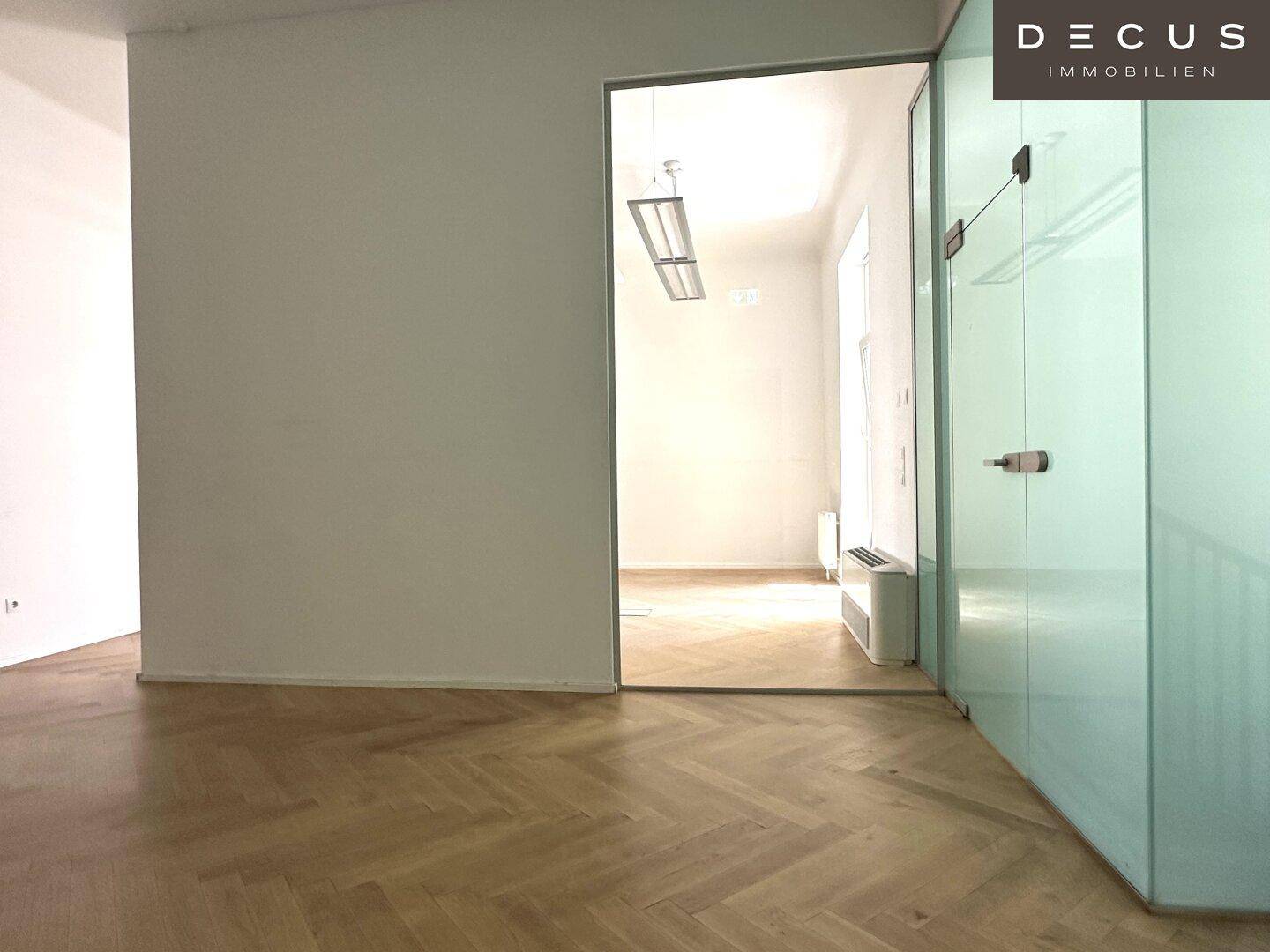 Offener Bürobereich mit Fischgrätparkett und einer Trennwand aus Milchglas, die für Privatsphäre sorgt.