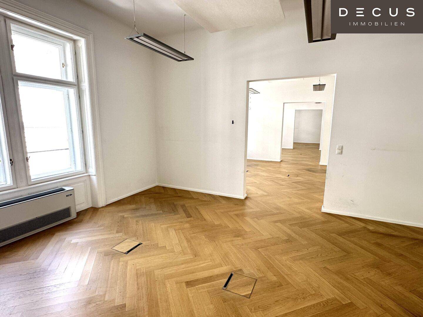 Offener Bürobereich mit Fischgrätparkett, großen Fenstern und mehreren Durchgängen, flexibel gestaltbar.