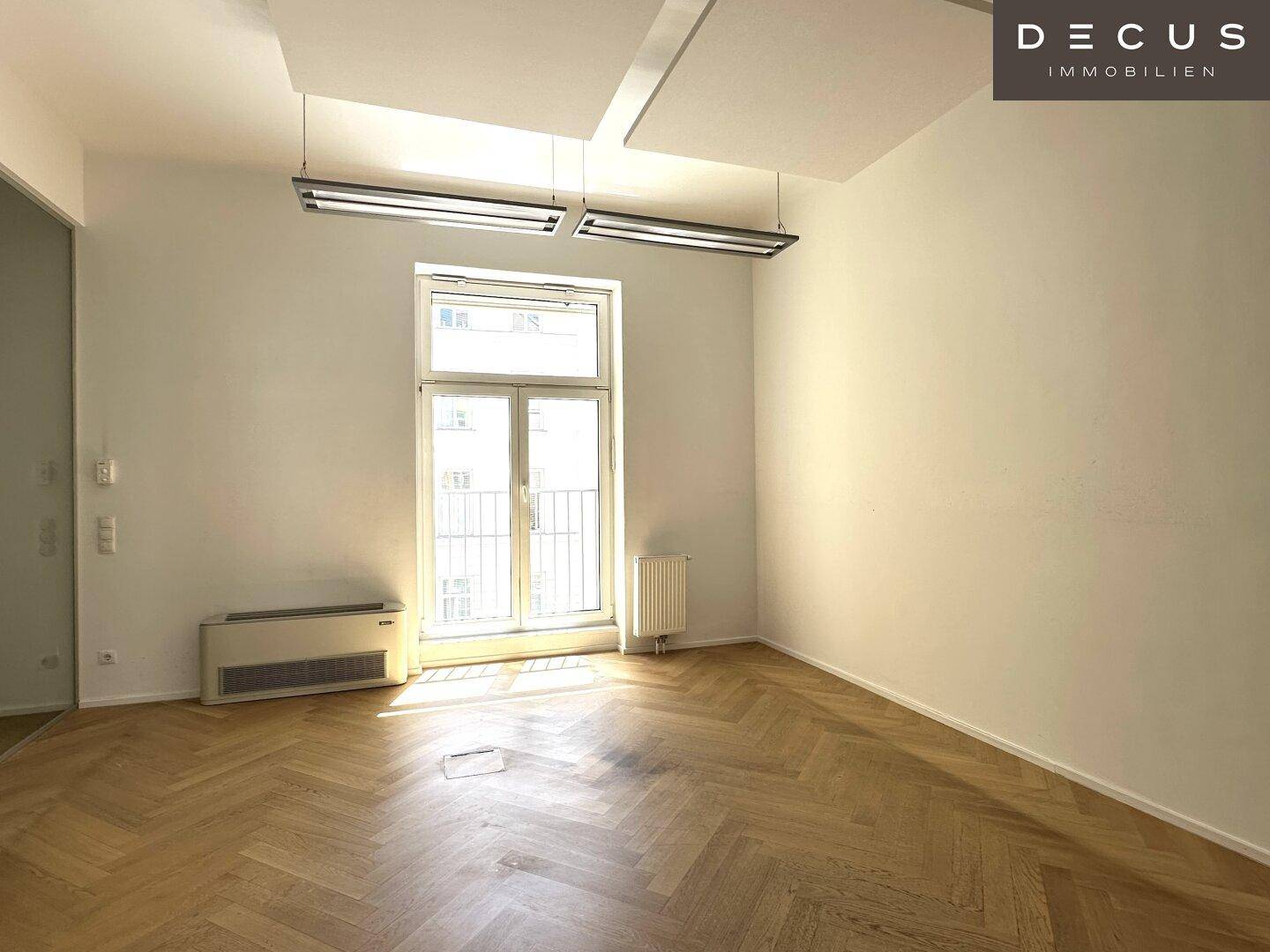 Heller Büroraum mit Fischgrätparkett, großen Fenstern und Zugang zu einem kleinen Balkon, ideal für Pausen.