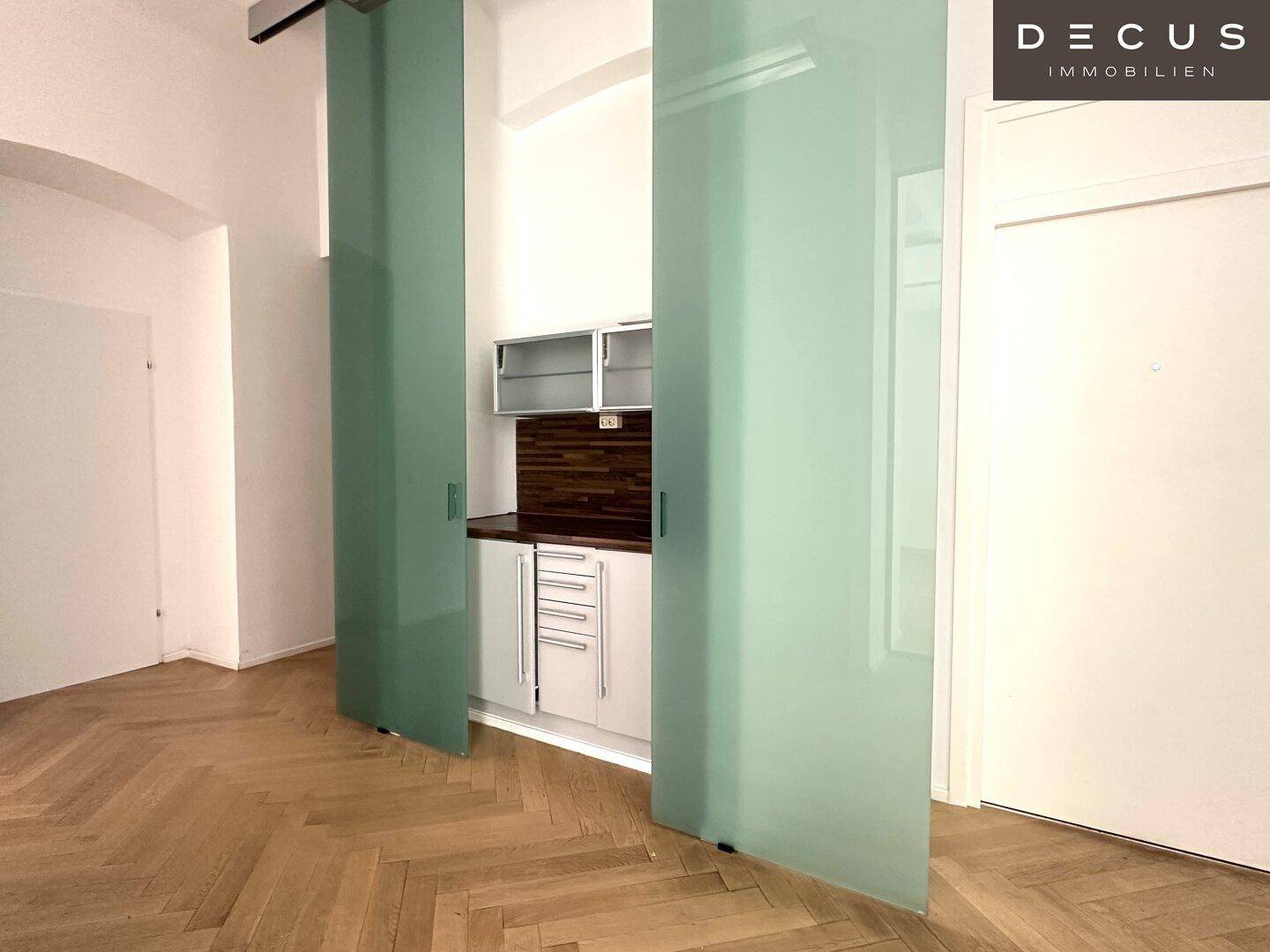 Versteckte Küchenzeile hinter Milchglasschiebetüren mit Holz-Arbeitsplatte und Oberschränken, platzsparend und modern.