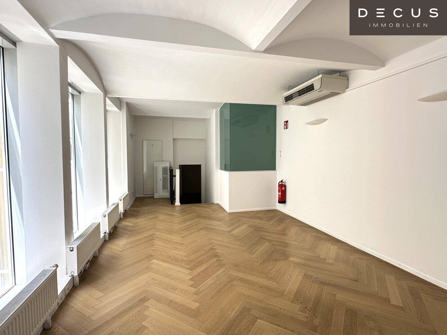 Großer Büroraum mit Fischgrätparkett, hohen Decken und Klimaanlage, ideal für ein angenehmes Arbeitsklima.