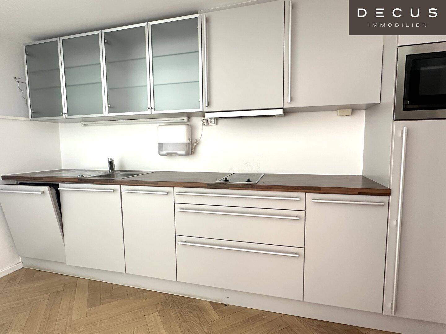 Moderne Küchenzeile mit weißen Schränken, Holz-Arbeitsplatte und integrierten Geräten, sehr funktional und kompakt.